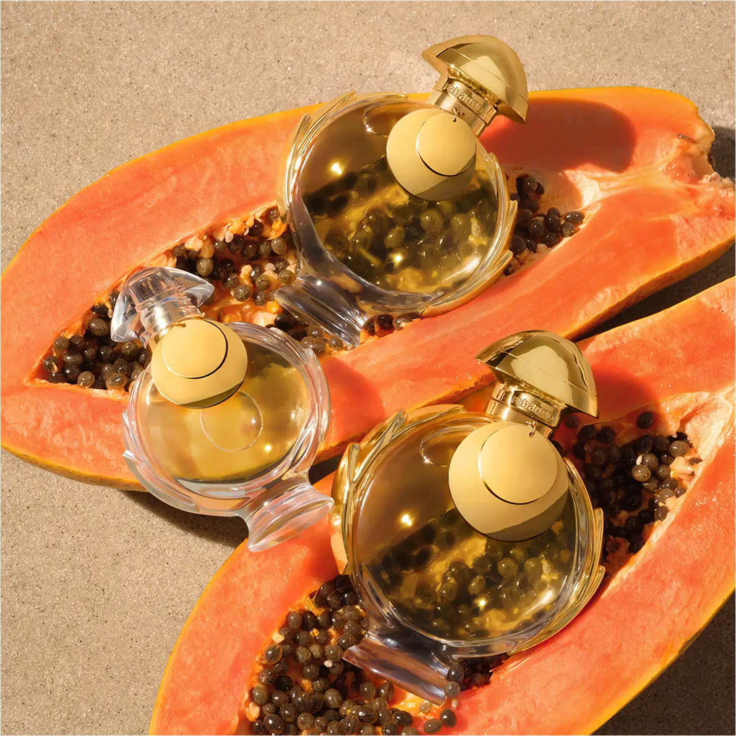 Três frascos de item de perfumaria dourados sobre fatias de mamão papaia laranja em um fundo bege. Os frascos têm tampas douradas e contêm um líquido dourado. 