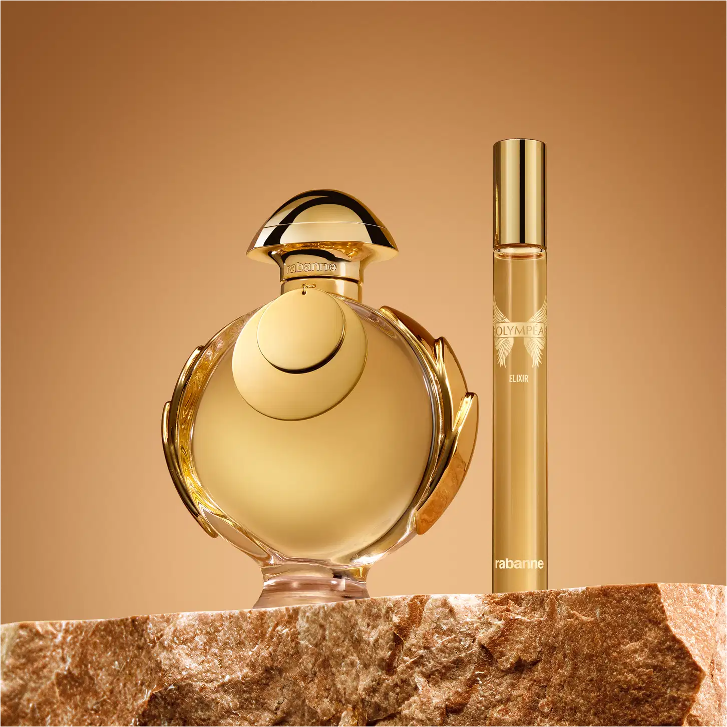 Ambiente de exibição de item de perfumaria da marca Olympea, com frasco de vidro dourado e tampa arredondada, acompanhado de um frasco menor, sobre superfície de pedra marrom em fundo laranja.