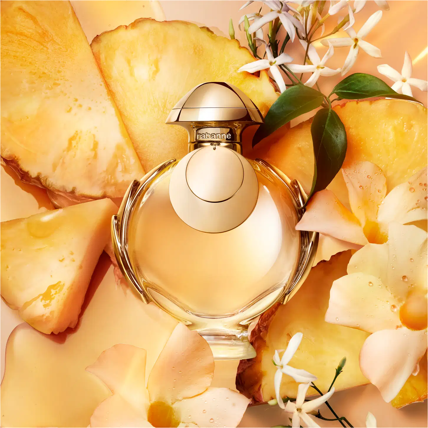 Recipiente de item de perfumaria Trabanne em primeiro plano, rodeado por fatias de abacaxi amarelo-dourado e flores brancas. 