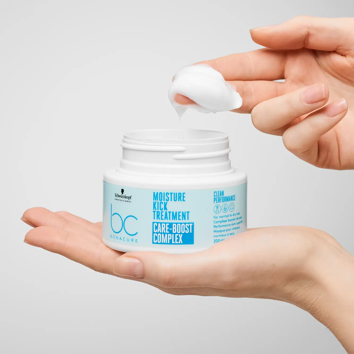 Mãos segurando um pote branco de tratamento capilar da marca Schwarzkopf Professional, com design minimalista e cores claras, em um ambiente limpo e iluminado, sugerindo um contexto de cuidados com a beleza e a saúde dos cabelos.