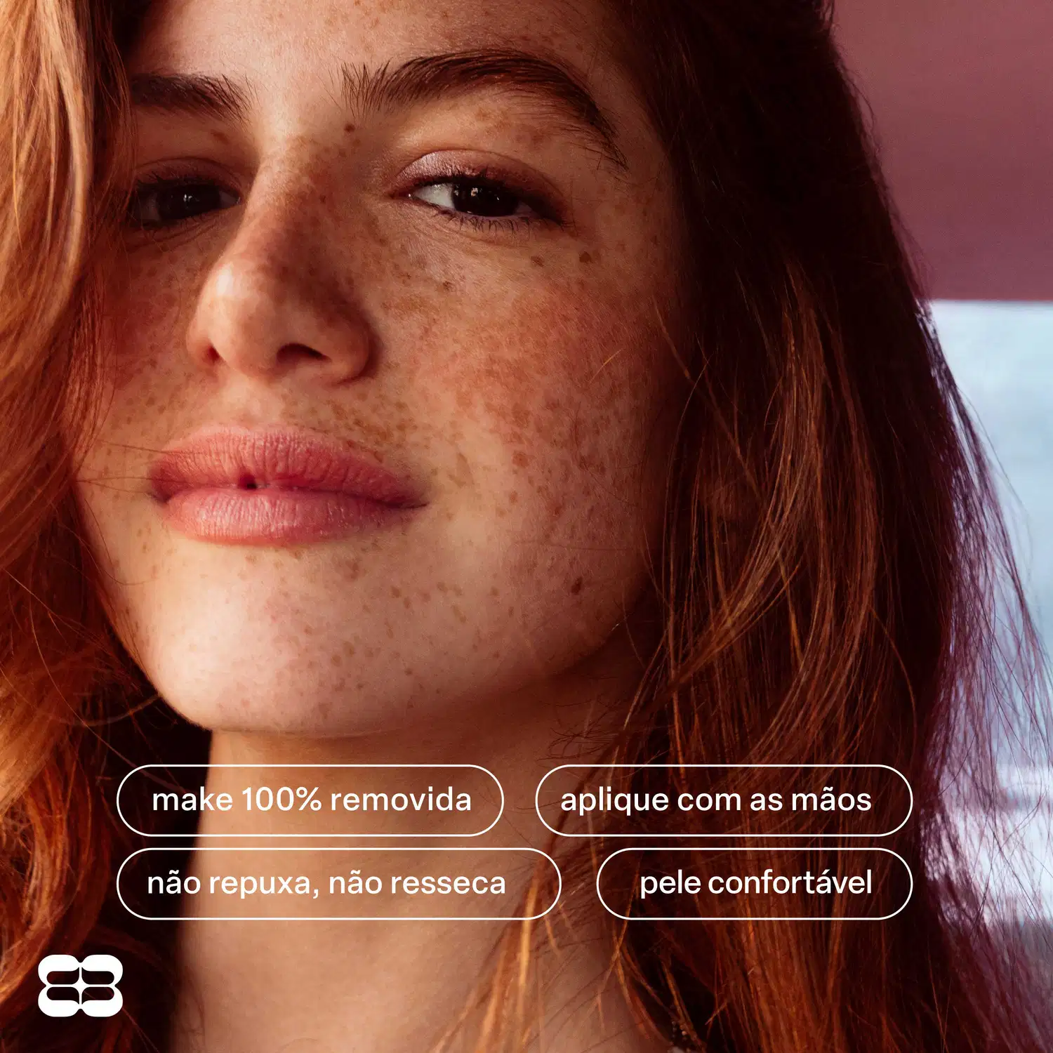 Rosto de mulher com cabelos ruivos e sardas, com texto "make 100% removida", "aplique com as mãos", "não repuxa, não resseca" e "pele confortável".