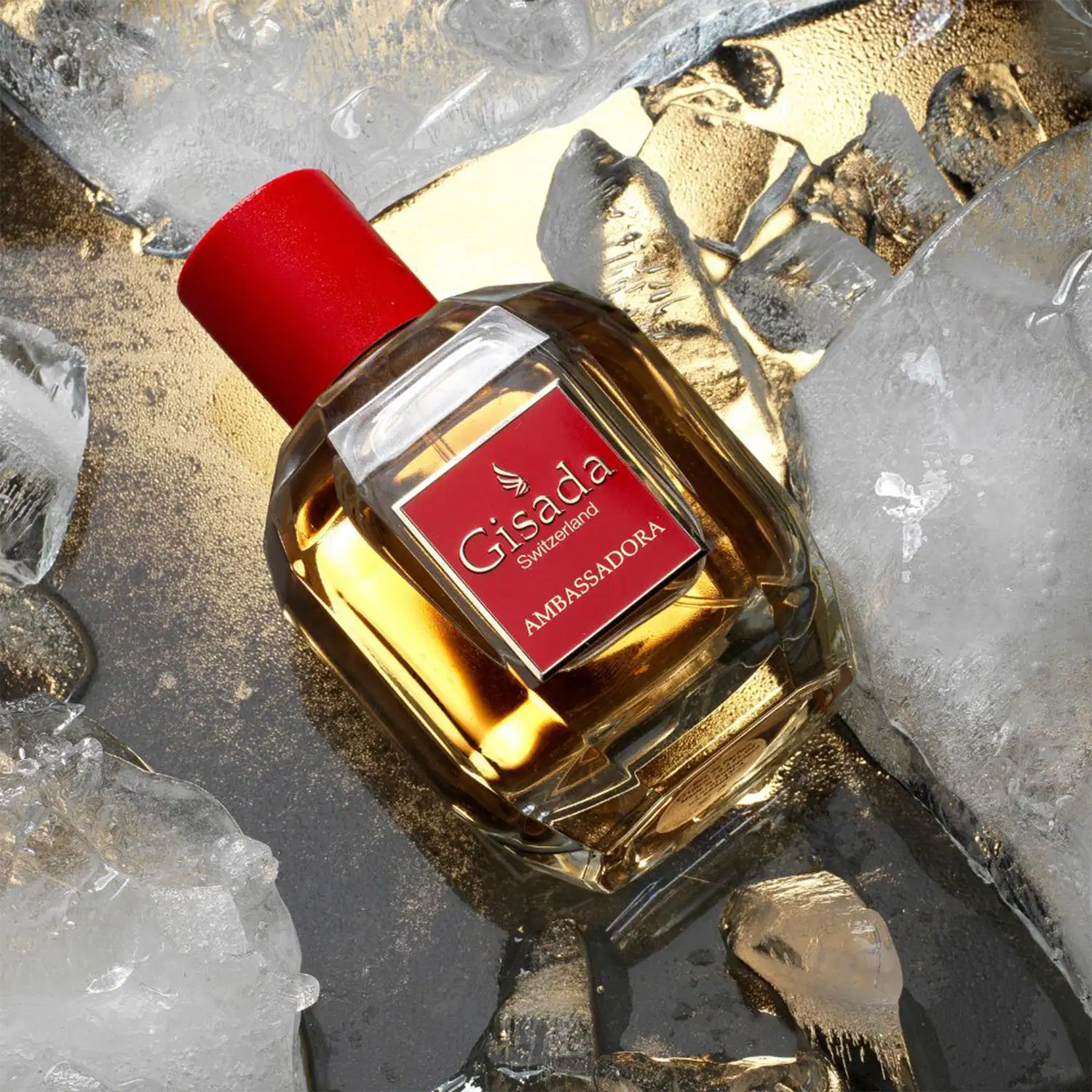 Frasco de item de perfumaria Gisada Ambassadora com tampa vermelha, posicionado sobre superfície com areia dourada e gelo, cercado por cubos de gelo e pedras.