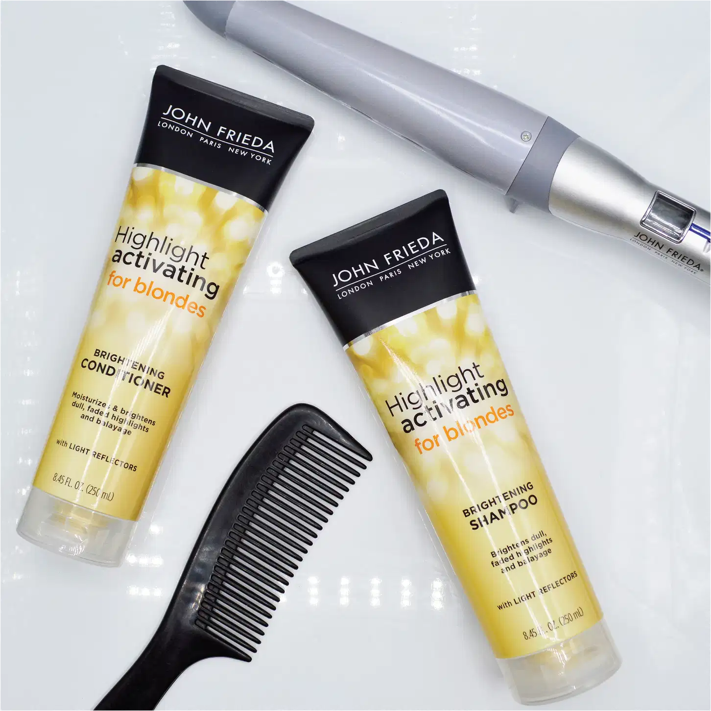 Imagem do shampoo e do condicionador da linah deitados em uma superfície plana da cor branca. Ao redor um pente preto e um modelador de cachos.