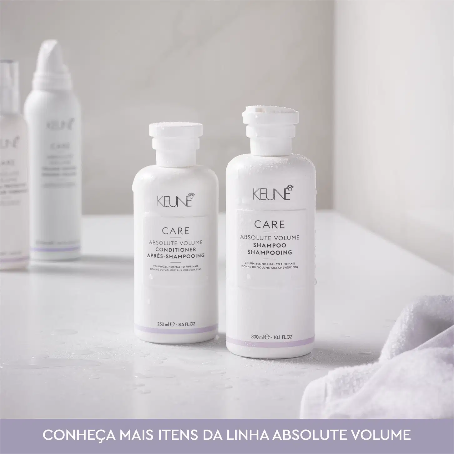 Dois frascos brancos da linha Absolute Volume da Keune, um contendo condicionador e outro shampoo, com rótulos e logotipos da marca. Os produtos são apresentados em embalagens de plástico branco com detalhes em roxo.