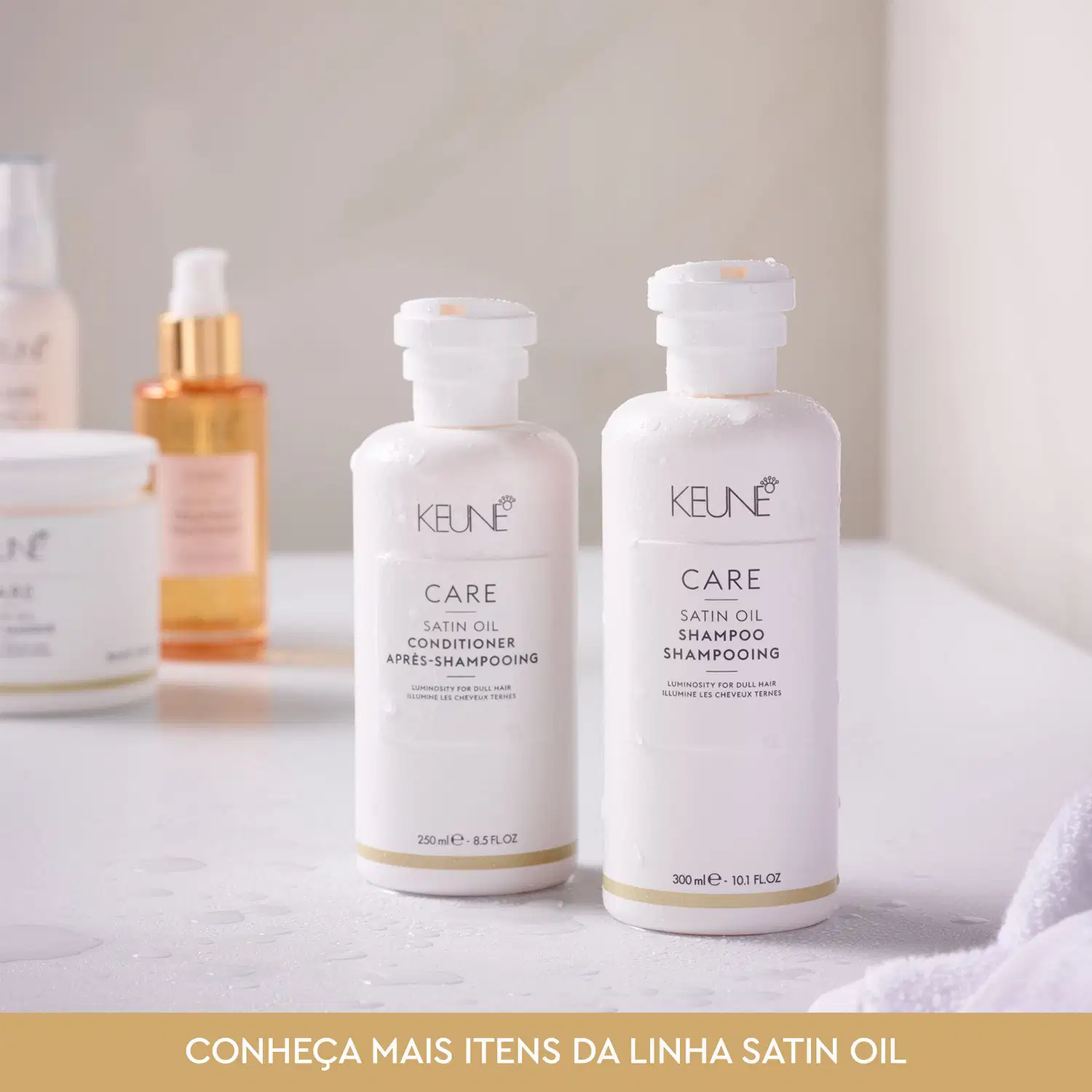 Dois frascos brancos da linha Satin Oil da Keune, um contendo condicionador e outro shampoo, com rótulos em branco e dourado destacando a marca e o nome da linha.