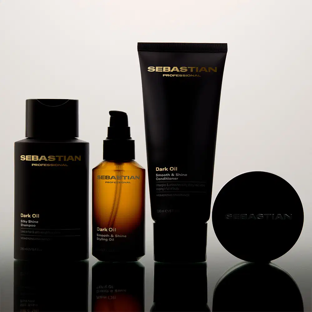 Produtos da marca Sebastian Professional, incluindo shampoo, óleo e condicionador da linha Dark Oil, em embalagens pretas e douradas, dispostos sobre uma superfície refletiva em um ambiente minimalista e monocromático.