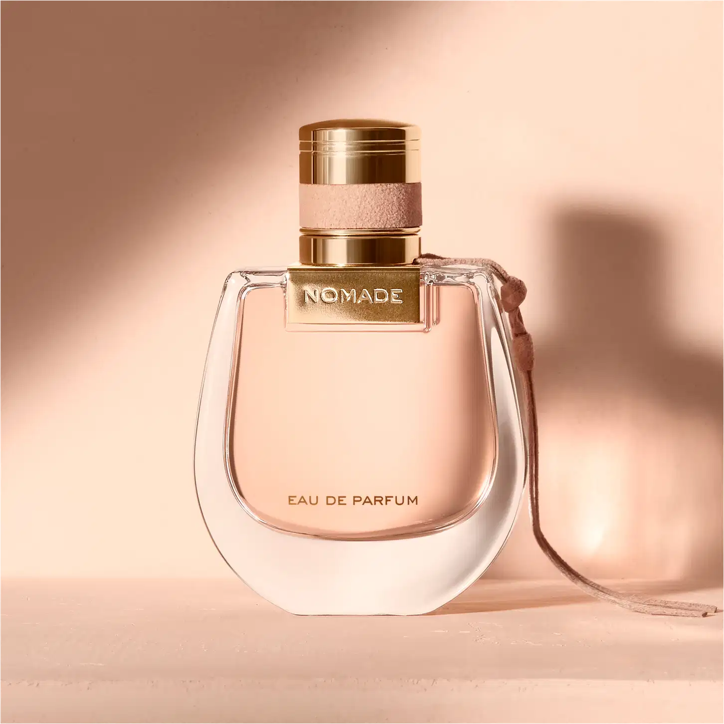 Perfume em um ambiente rosado, com uma luz sobre o frasco projetando uma sombra na parede.