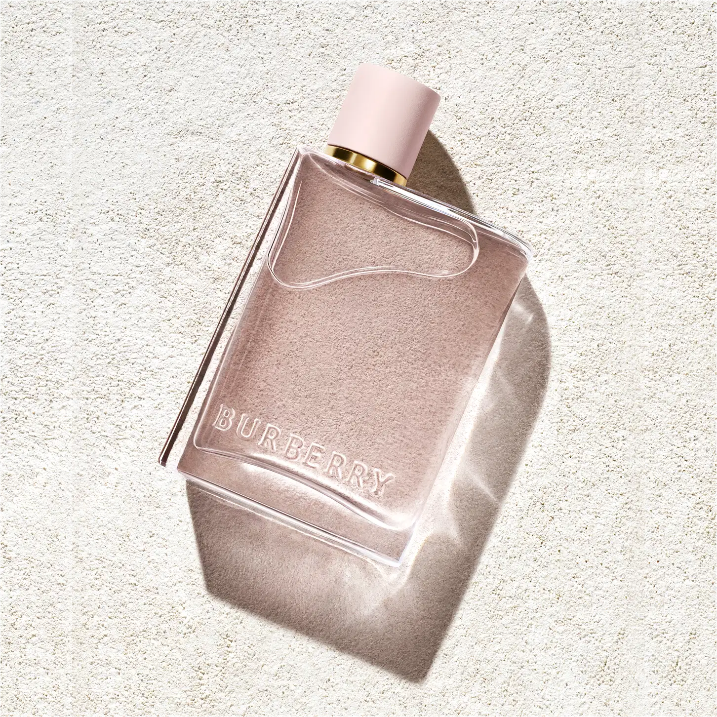 Frasco de perfume Burberry de cor rosa pálido com tampa dourada. O rótulo em destaque exibe o nome da marca "BURBERRY" em letras brancas.