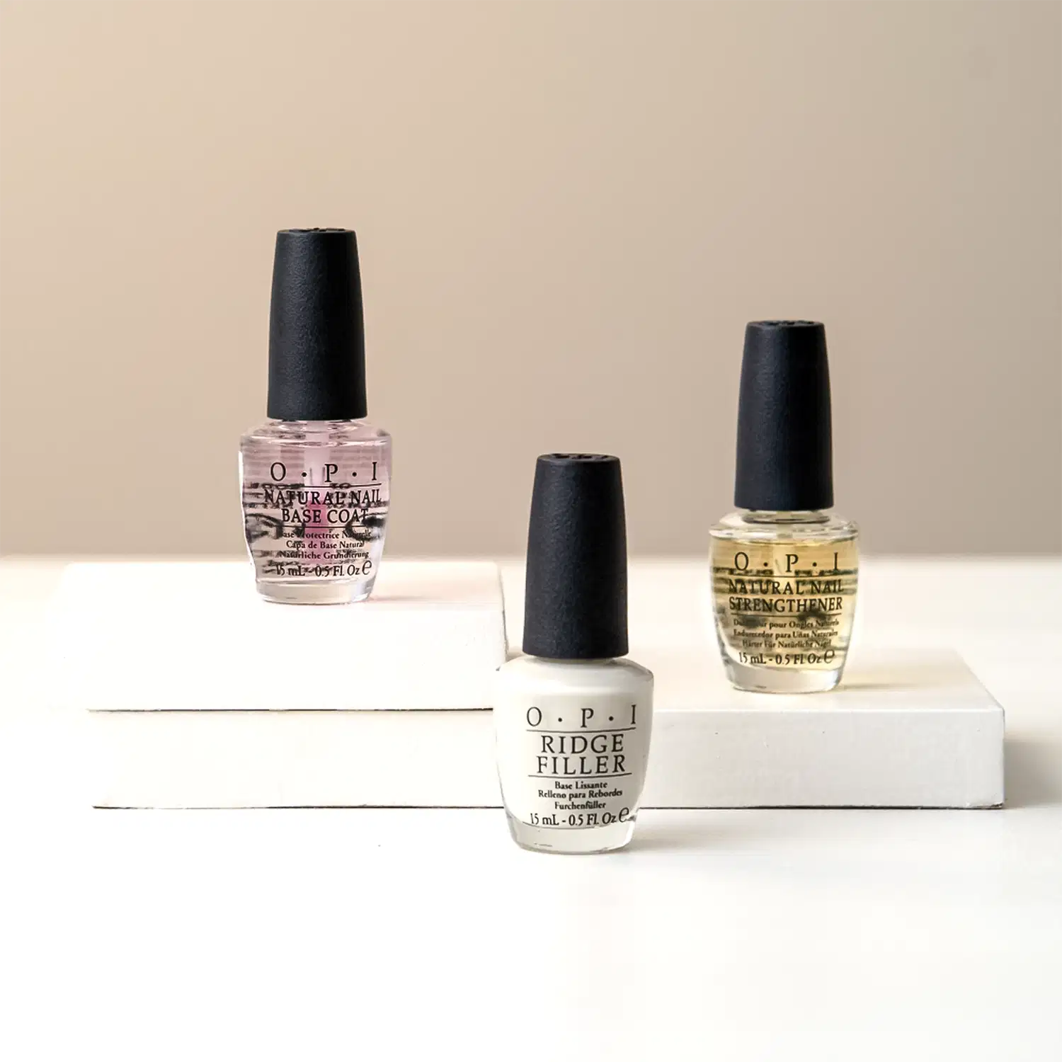 Três frascos de produtos para unhas da marca OPI. Os produtos estão dispostos sobre uma superfície clara.
