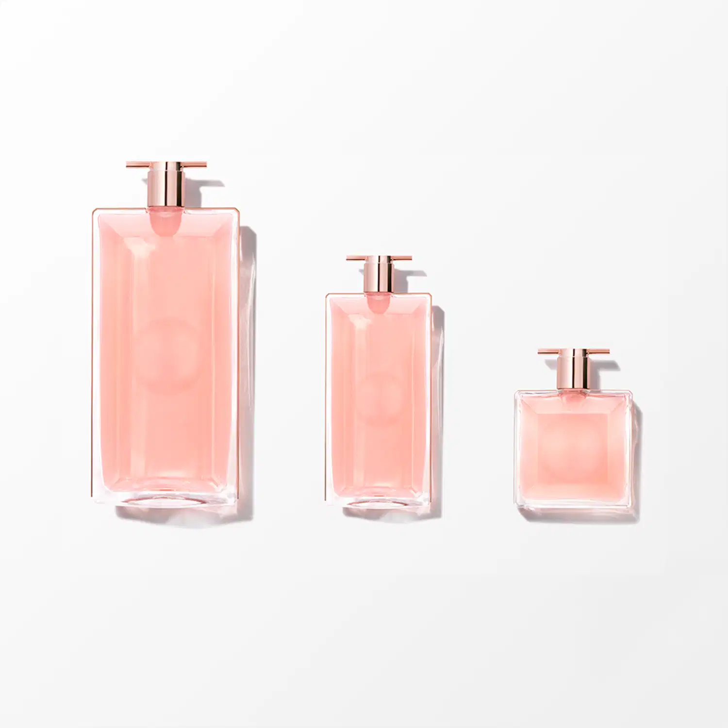 Três frascos de perfume Lancôme em diferentes tamanhos, com embalagens de vidro rosa translúcido e detalhes em metal rosé. Os frascos possuem formatos geométricos elegantes e simétricos, com bombas doseadoras no topo.