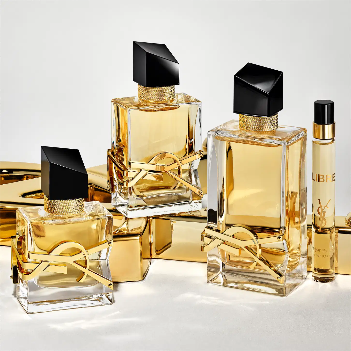Fragrâncias Yves Saint Laurent em embalagens de vidro e metal dourado, com detalhes pretos e rótulos destacados. Diversos frascos de diferentes tamanhos e formatos, exibindo a marca e o nome dos produtos.