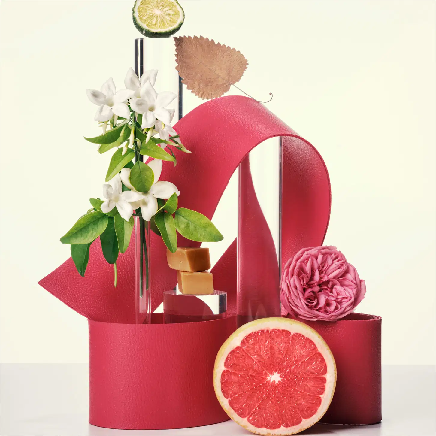 Ambiente elegante e sofisticado com elementos florais, cítricos e acessórios em tons de rosa, vermelho e verde, sugerindo um produto de beleza da marca Carolina Herrera.