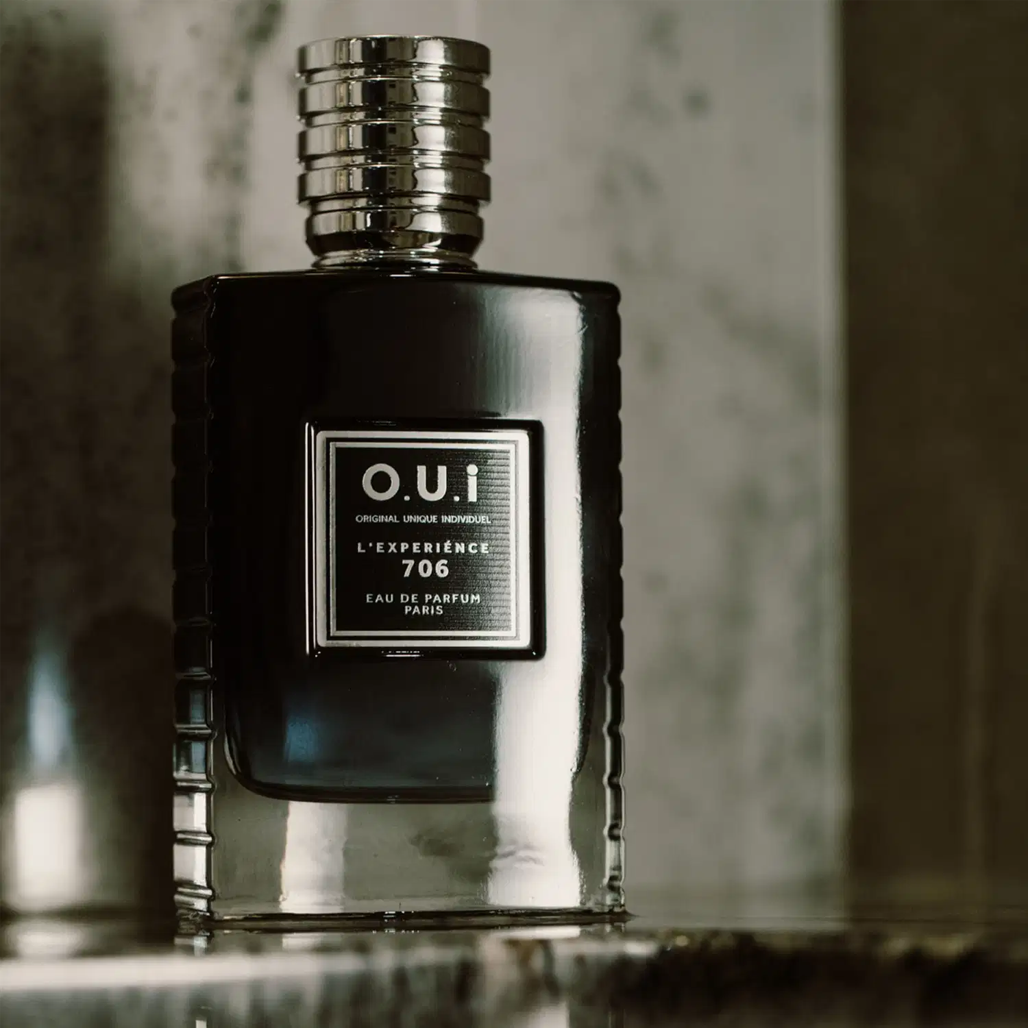 Um item de perfumaria preto com rótulo branco e texto em francês, posicionado em um ambiente escuro e sombrio, sugerindo um contexto elegante e sofisticado para seu uso.