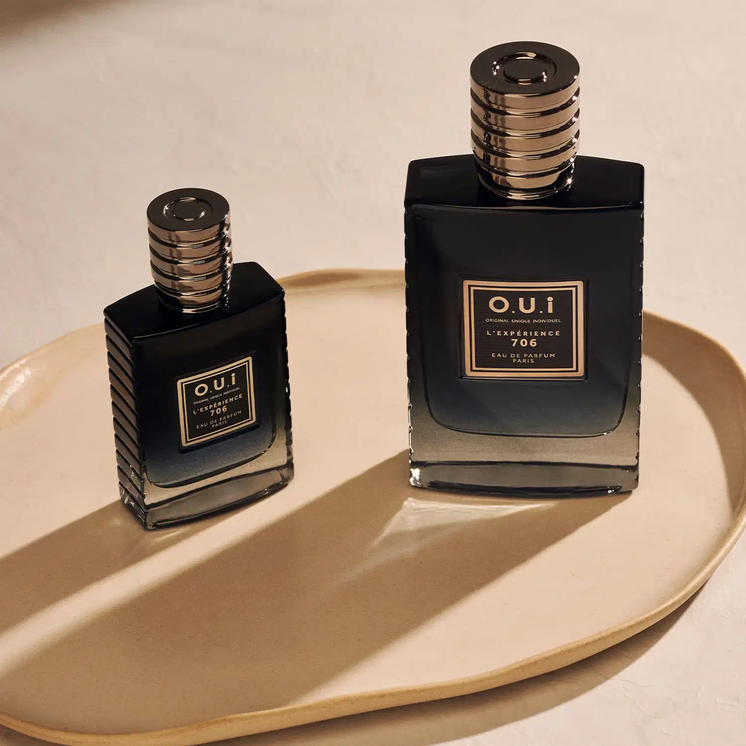 Dois frascos de item de perfumaria da marca O.U.I. em uma bandeja dourada. Os frascos possuem design elegante com detalhes em preto e dourado, indicando tratar-se de uma fragrância sofisticada. O ambiente sugere um cenário de luxo e exclusividade.