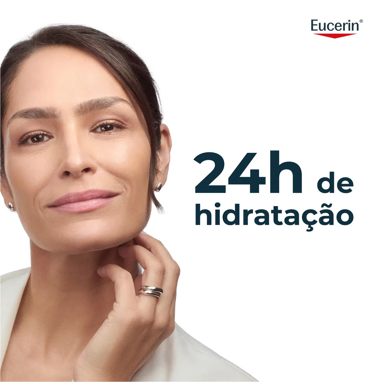 Uma mulher madura com cabelos escuros e expressão séria, com a marca Eucerin visível no canto superior direito da imagem, que apresenta o texto "24h de hidratação" em destaque.