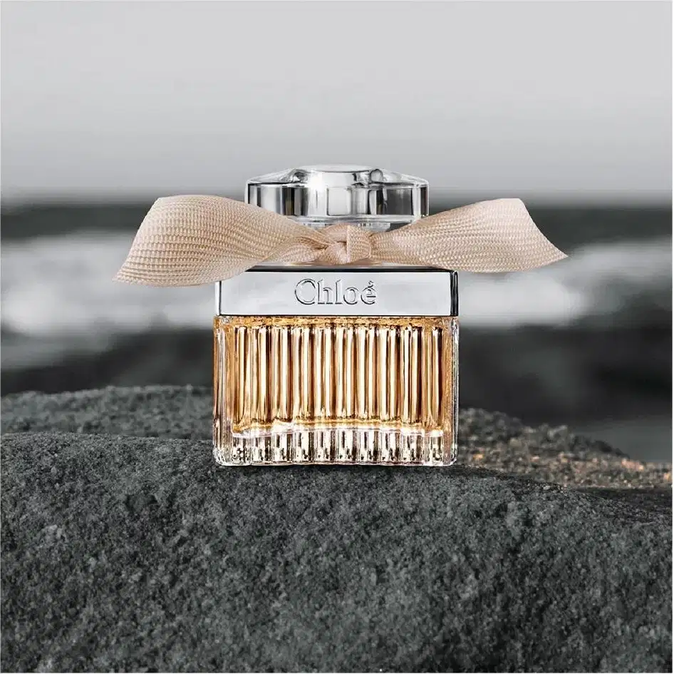 Frasco de perfume Chloé com tampa prateada e laço bege, apresentando o nome da marca em destaque. O design elegante e minimalista transmite sofisticação.