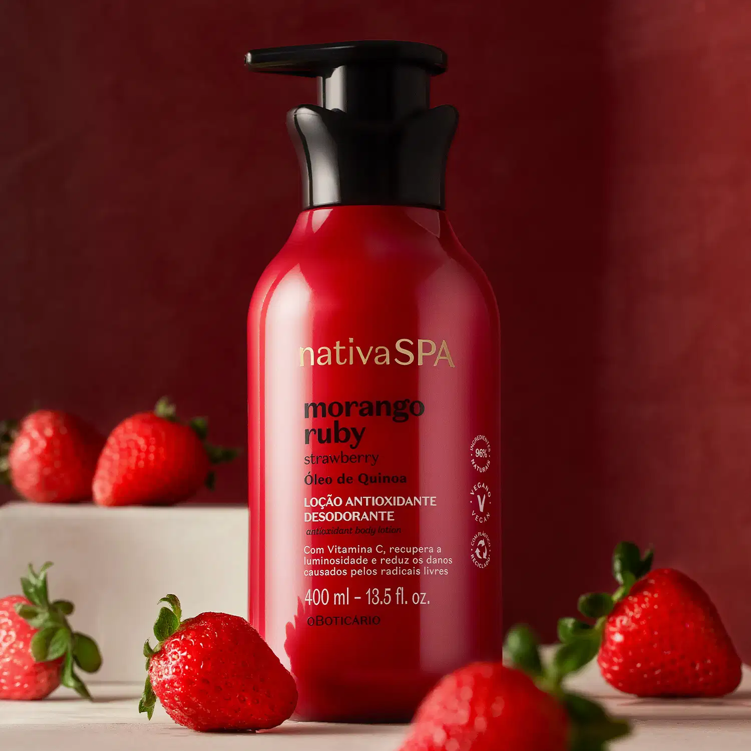 Frasco vermelho com bomba dosadora preta e letras douradas, brancas e pretas de loção antioxidante corporal Nativa SPA Morango Ruby, cercado por morangos frescos sobre superfície branca e fundo vermelho escuro.