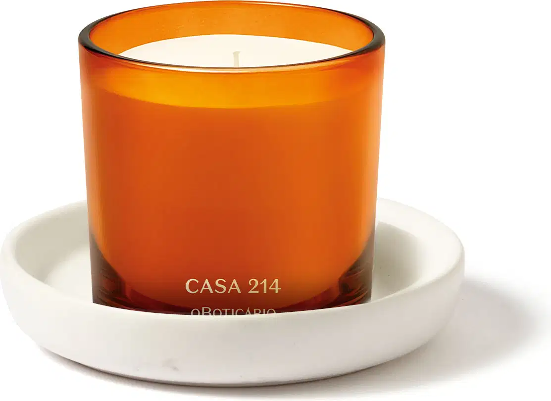 Vela perfumada da marca Casa 214 Vanilla Sublime em recipiente laranja e vela branca aromatizada acompanhada de um suporte para velas na cor branca.