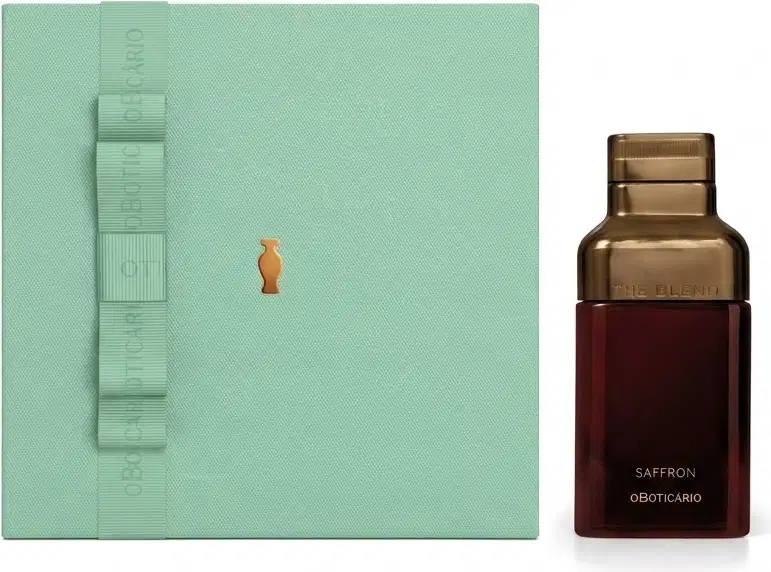 Caixa de presente verde-clara com fita no mesmo tom e o Boticário em dourado. Ao lado, vemos um frasco de vidro marrom com rótulo em letras douradas escrito "Saffron".