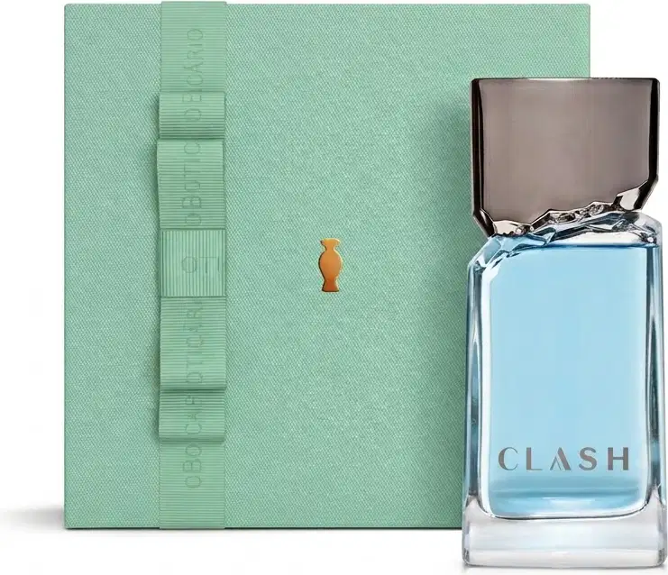 Caixa de presente verde-clara com fita no mesmo tom e o Boticário em dourado. Ao lado, vemos um frasco de vidro transparente com líquido azul-claro e tampa preta da fragrância "CLASH".