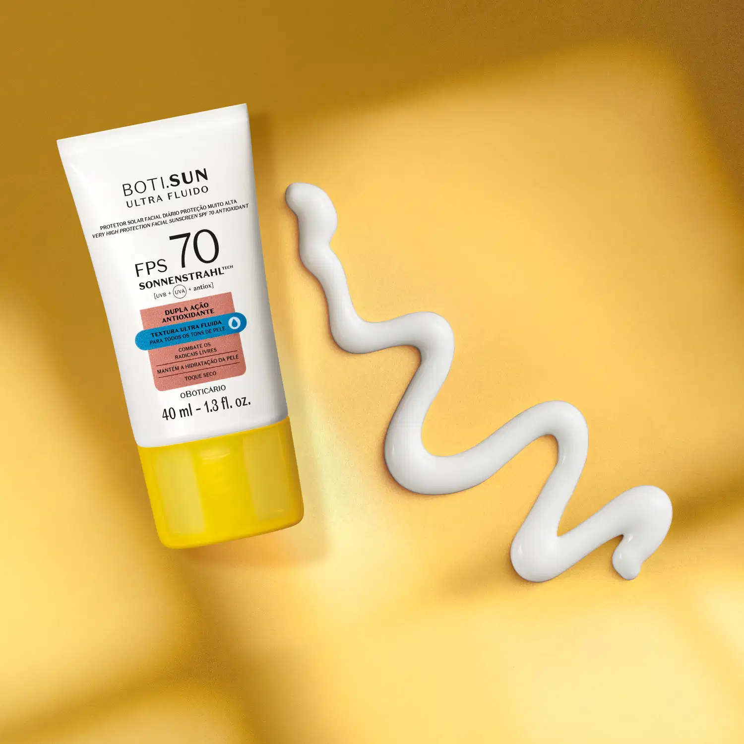 Frasco branco com tampa amarela, letras pretas e detalhes nas cores azul e laranja contendo protetor solar facial antioxidante FPS 70 Ultra Fluído da marca Boti.Sun em fundo laranja com sombra e uma pequena quantidade de creme branco ao lado.