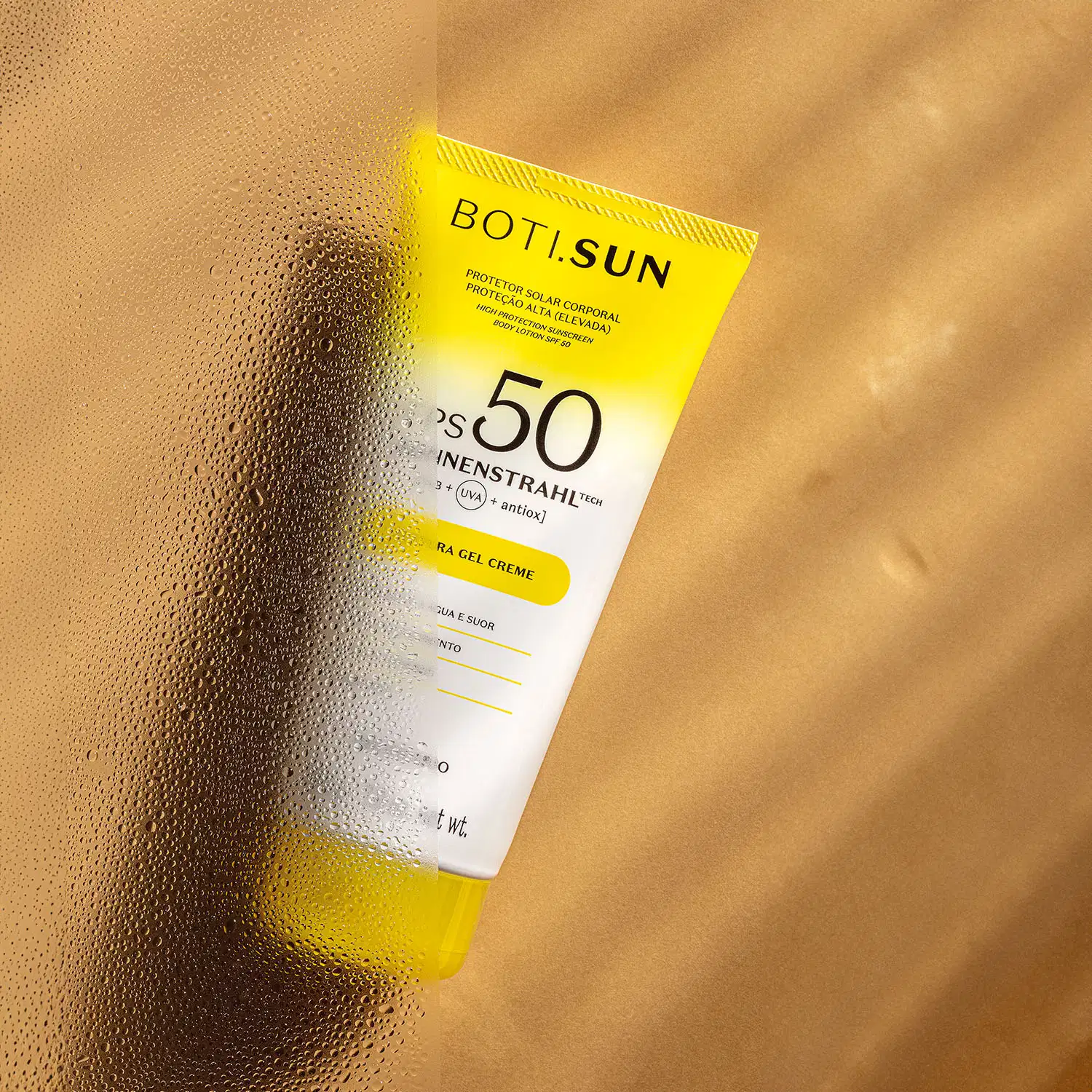 Bisnaga amarela e branca com tampa amarela e letras pretas contendo 200g de protetor solar corporal FPS 50 da marca Boti.Sun em um fundo bege com sombras onduladas.