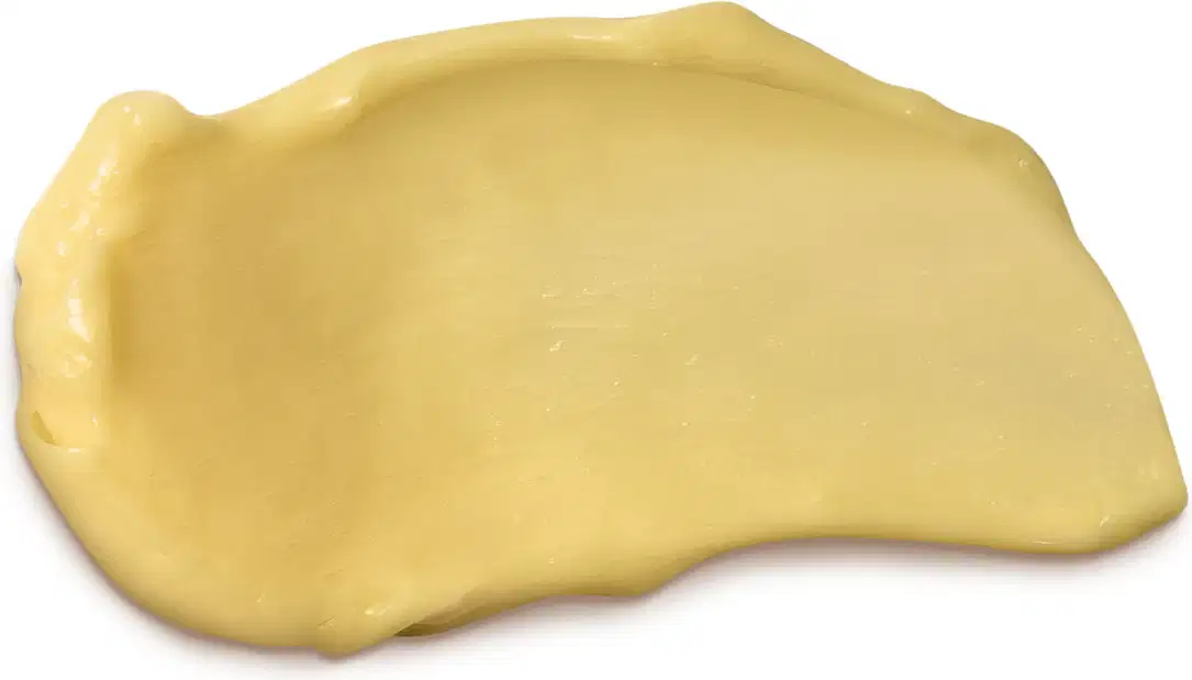 Textura cremosa e amarelada de condicionador da marca Cuide-se Bem Feira Banana, com aparência densa e uniforme, espalhada em superfície branca e lisa.