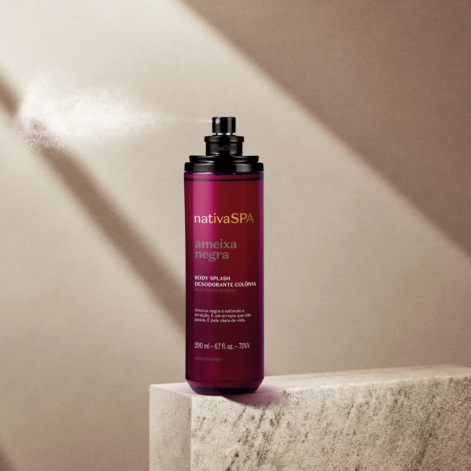 Frasco cilíndrico roxo transparente com tampa preta e letras douradas, brancas e roxas, contendo 200ml de body splash Nativa SPA Ameixa Negra, posicionado em superfície de concreto cinza claro, sob iluminação natural com sombras em parede bege.