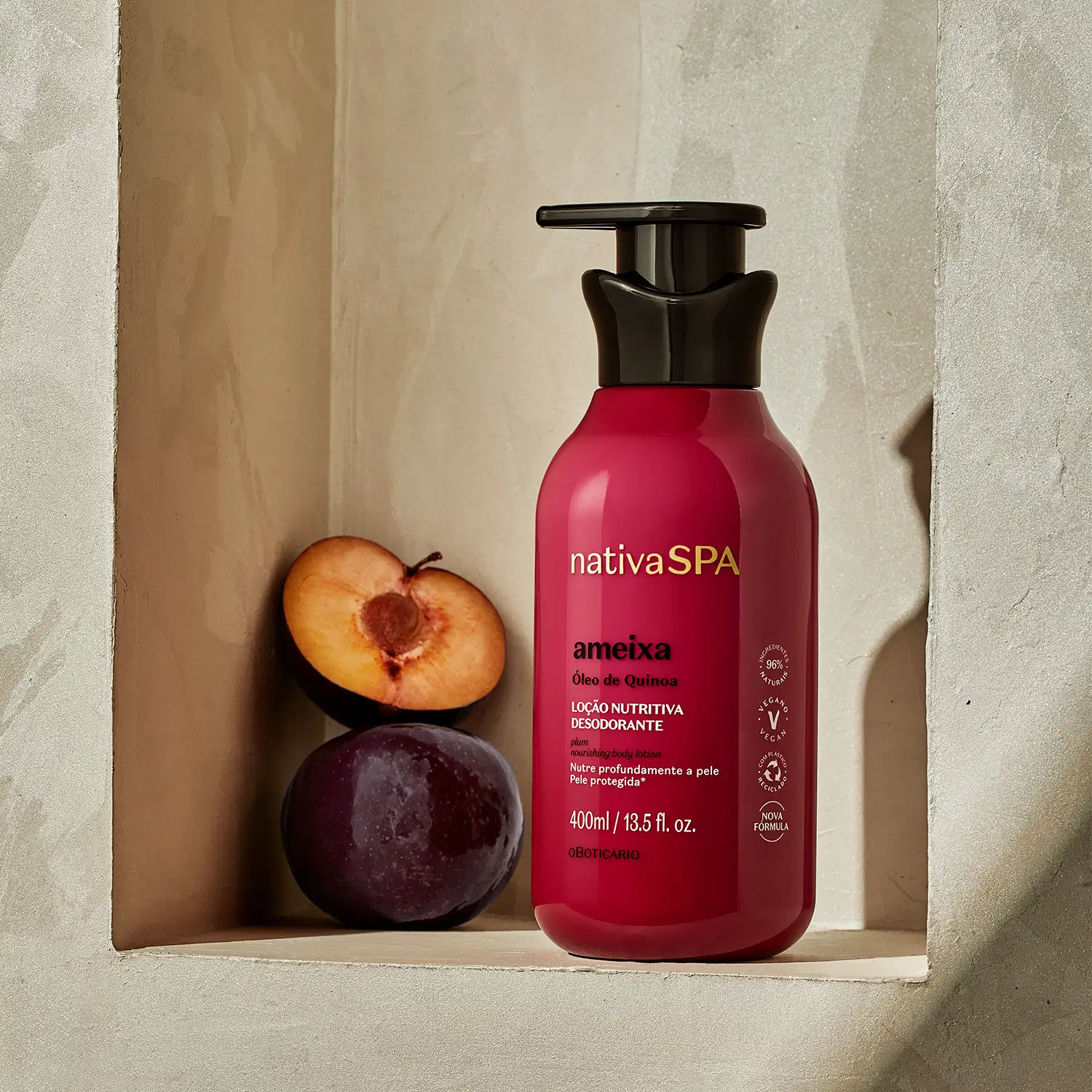 Frasco rosa vibrante com tampa dosadora preta e letras douradas, brancas e pretas de loção hidratante corporal Nativa SPA Ameixa. posicionado em nicho bege ao lado de meia ameixa fresca e ameixa inteira.
