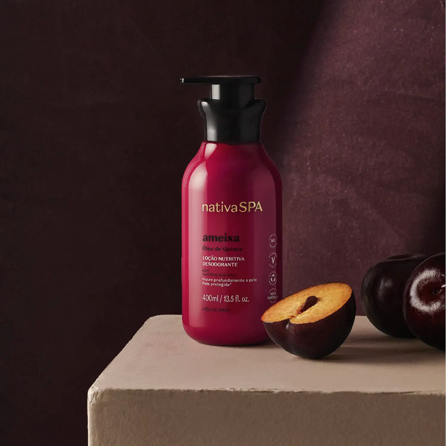 Frasco rosa vibrante com tampa dosadora preta e letras douradas, brancas e pretas de loção hidratante corporal Nativa SPA Ameixa sobre superfície bege, ao lado de ameixas pretas cortadas, com fundo marrom escuro.