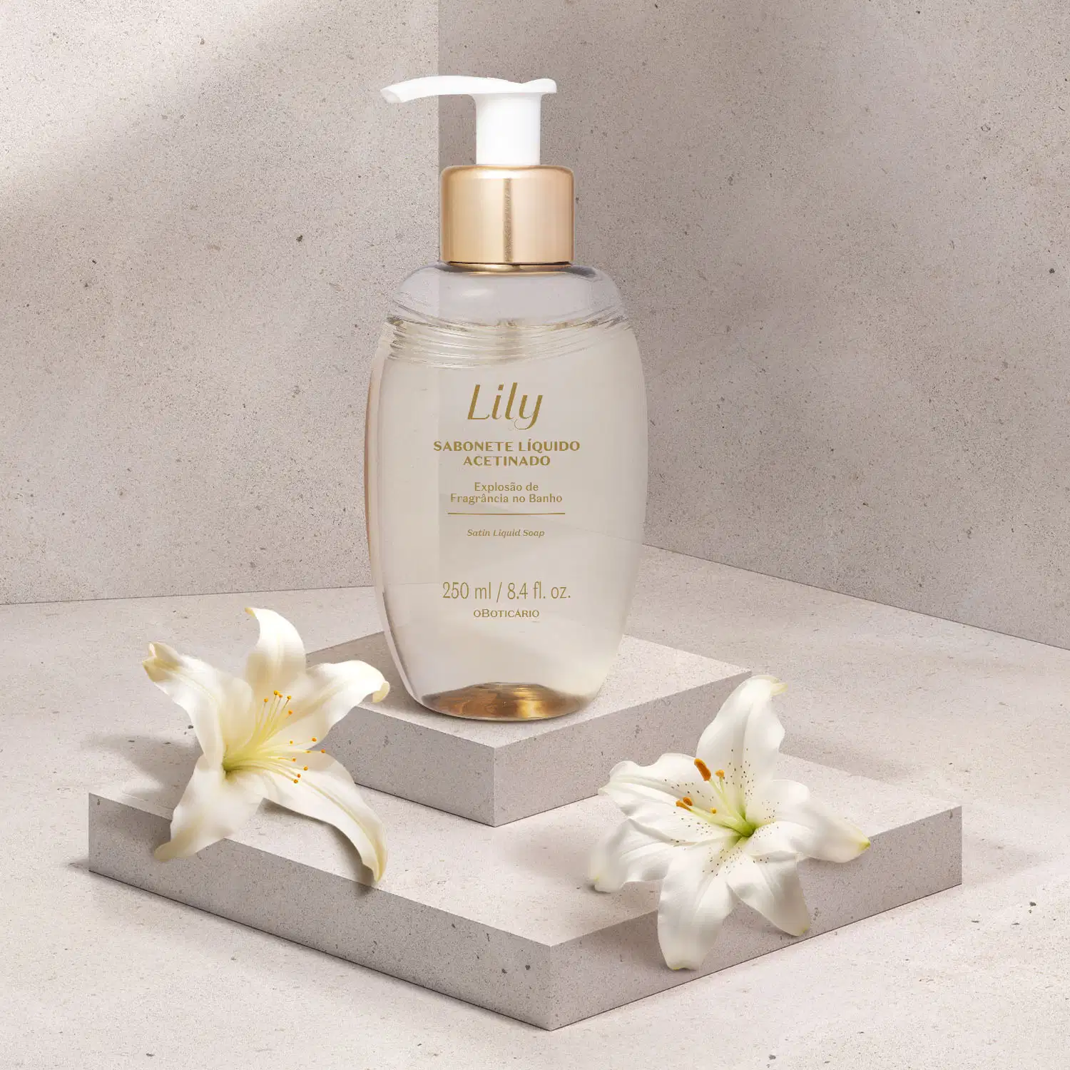 Frasco ovalado bege com letras marrons, detalhe dourado e bomba dosadora branca de sabonete líquido acetinado da marca Lily em uma plataforma branca, com flores brancas ao redor, em um cenário com fundo cinza.