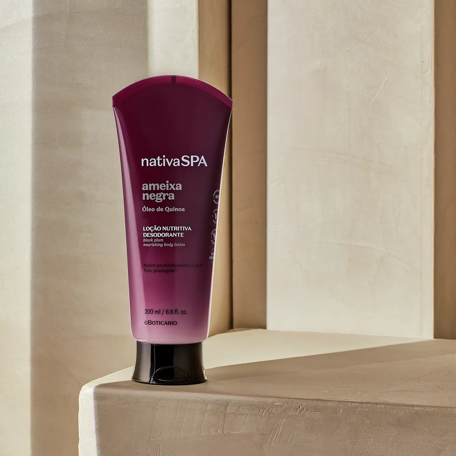 Bisnaga com degradê de roxo escuro e branco, tampa preta e letras douradas, brancas e pretas de loção nutritiva corporal da marca Nativa SPA Ameixa Negra. posicionado em superfície bege clara, com paredes e portas de madeira ao fundo em tons neutros.