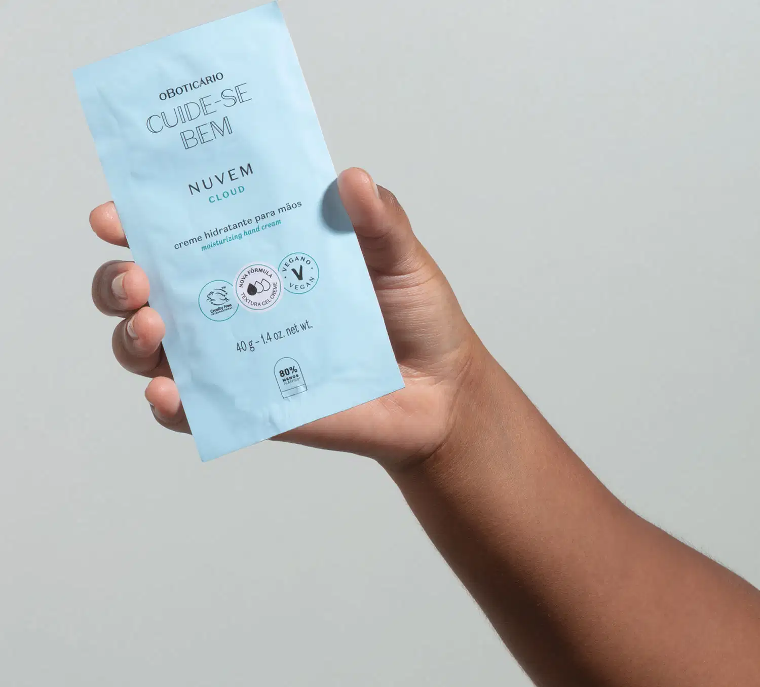 Mão segurando um refil de creme hidratante para as mãos da marca Cuide-se Bem Nuvem em sachê na cor azul com letras pretas e em fundo azul claro.