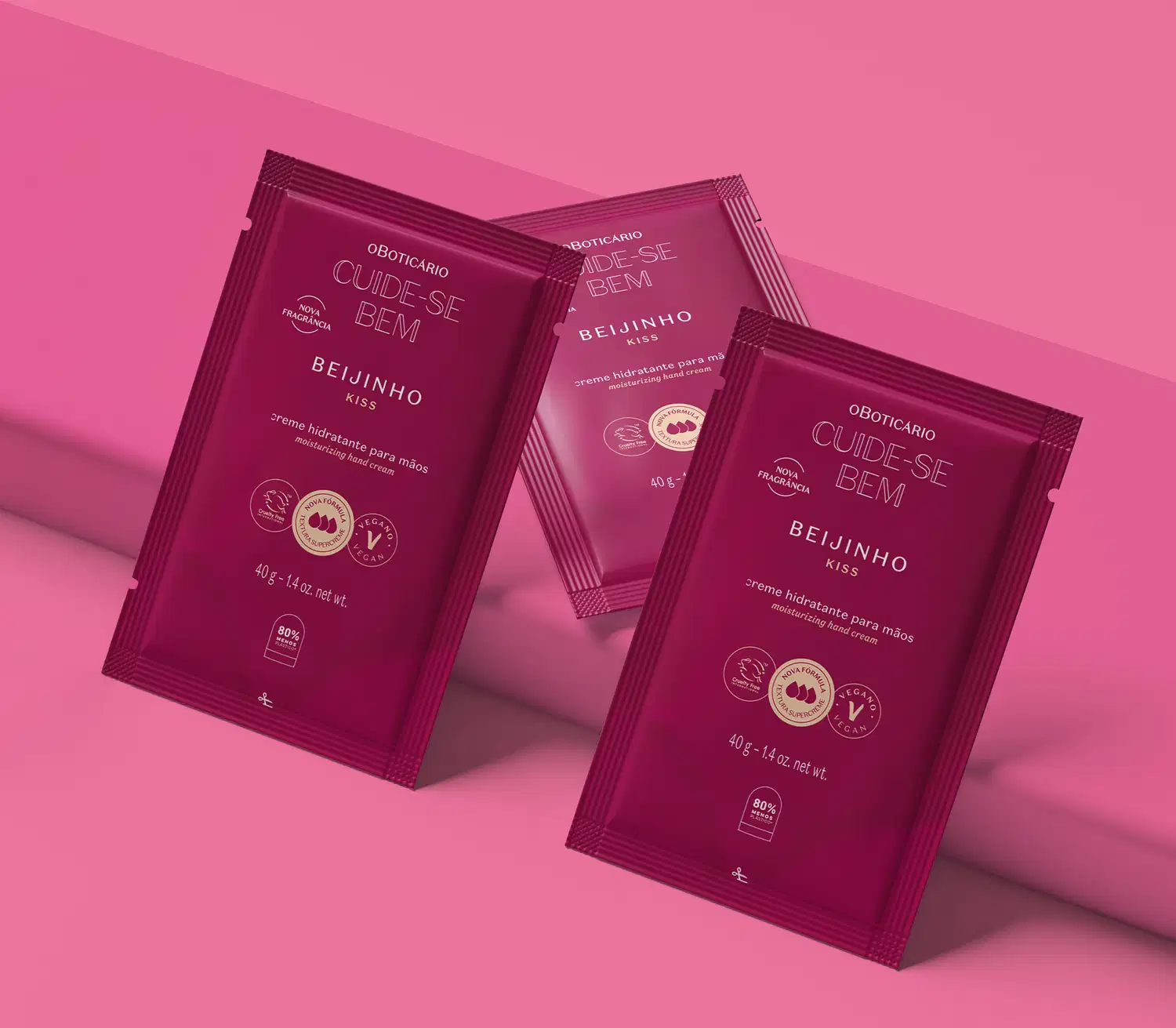Três refis de creme hidratante para as mãos da marca Cuide-se Bem Beijinho em sachês de 40g na cor vinho com letras bege. Eles estão em fundo rosa.