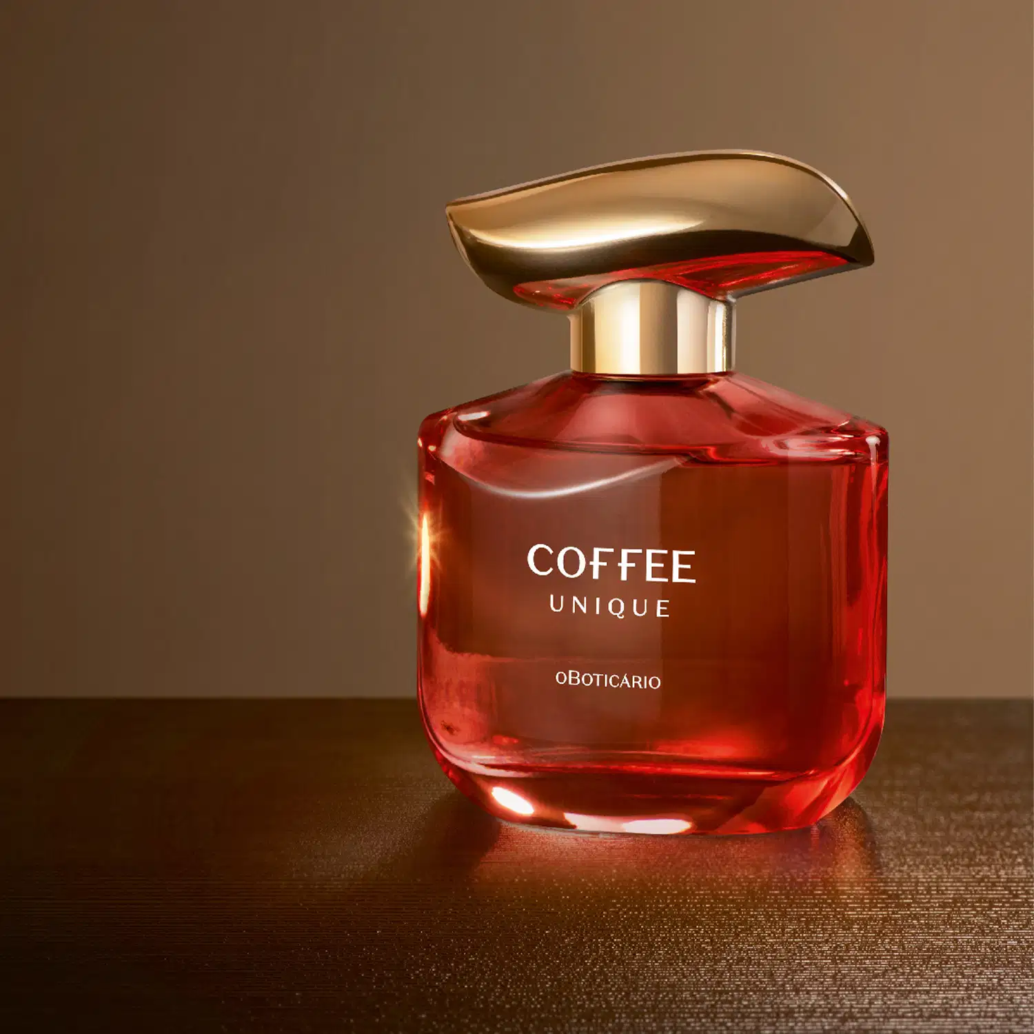 Imagem de um frasco de vidro avermelhado com tampa dourada de desodorante colônia da marca Coffee Woman Unique, em fundo marrom escuro, refletindo a luz em sua superfície brilhante e amadeirada.