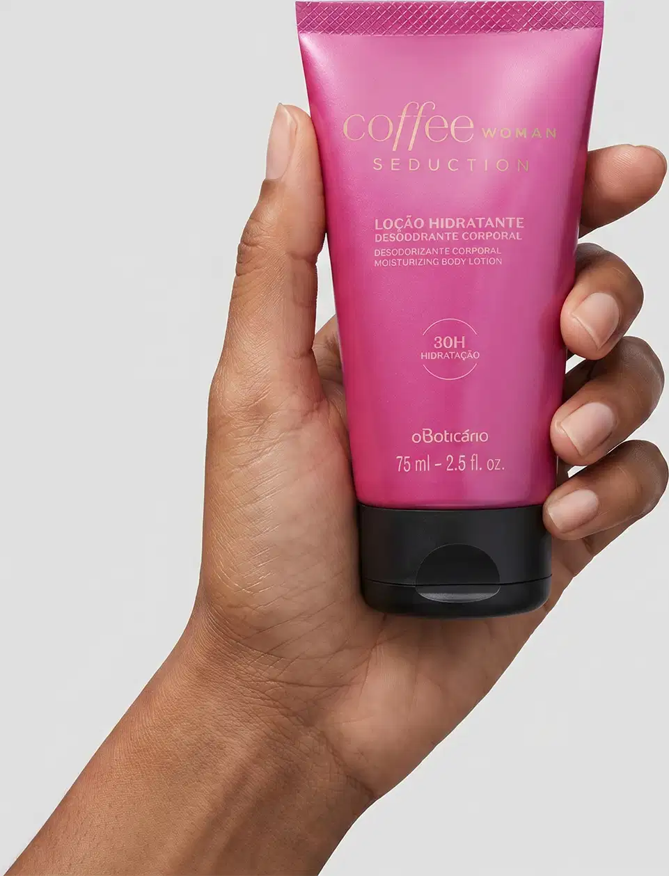 Recipiente de plástico rosa com rótulo "Coffee Woman Seduction" contendo loção hidratante desodorante corporal. O produto é segurado por uma mão feminina de pele negra em primeiro plano contra um fundo branco liso.