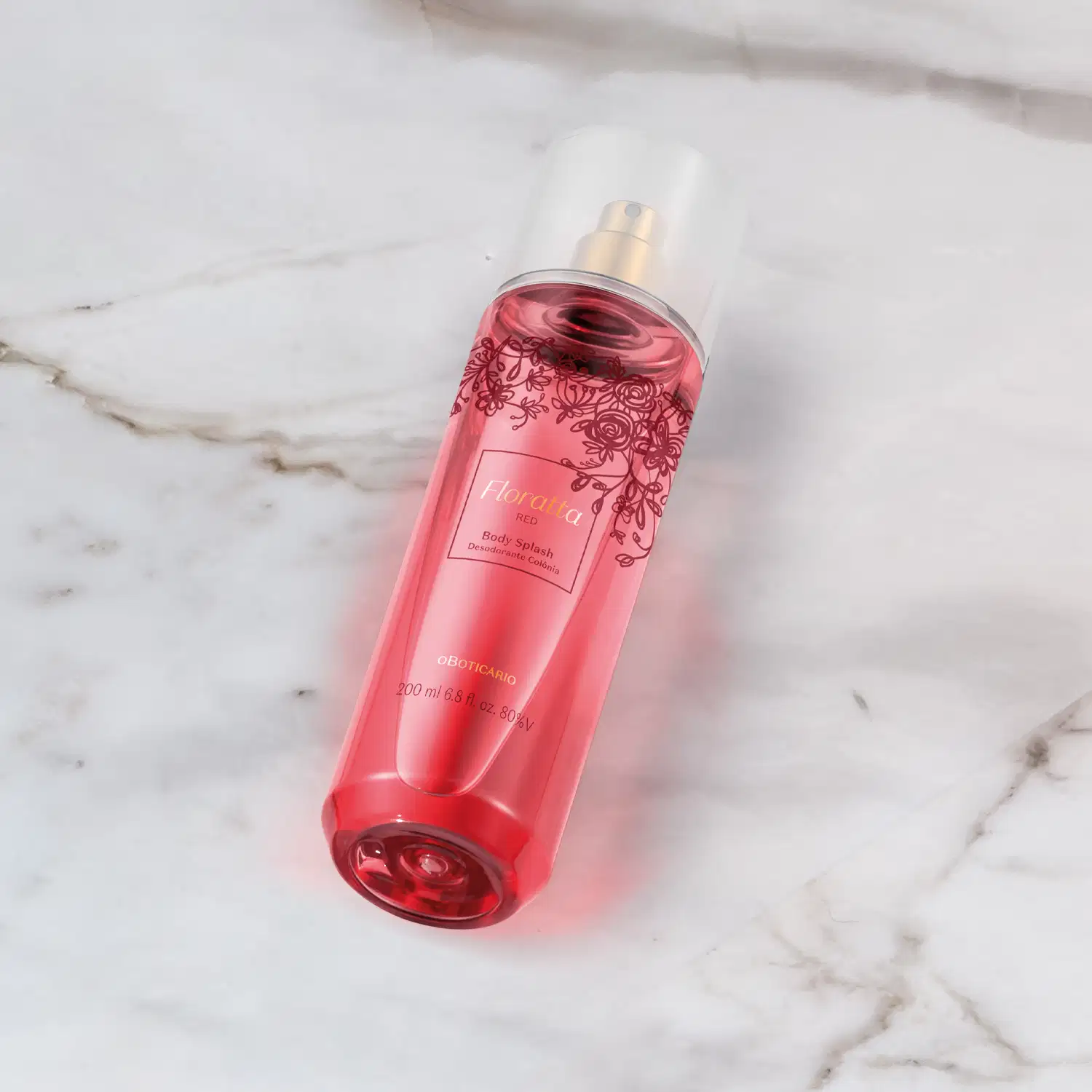 Frasco rosa com detalhes em vinho e letras douradas, pulverizador prateado e tampa cristal de body splash Floratta Red. posicionado sobre superfície de mármore branco com veios cinzas.