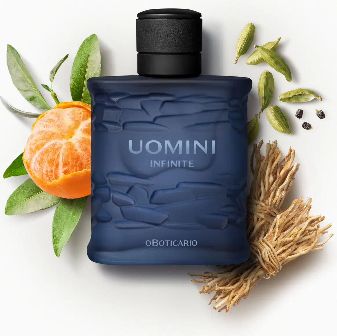 Frasco retangular azul marinho com texturas onduladas, tampa preta e letras com degradê em tons de azul de desodorante colônia da marca Uomini Infinite rodeado por gomos de bergamota, folhas verdes, vagens de cardamomo e raízes secas.