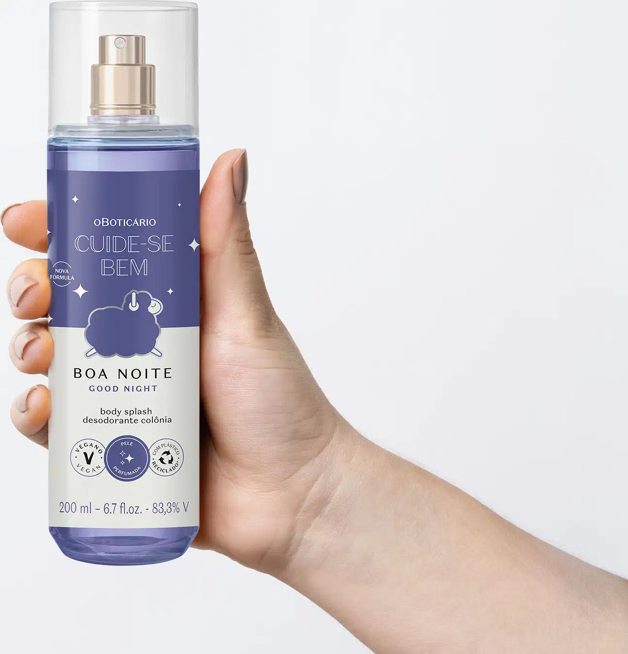 Mão segurando um Frasco com líquido azul claro, pulverizador prateado, tampa transparente e rótulo azul escuro e branco com ovelhinha ilustrada de body splash da marca Cuide-se Bem Boa Noite em fundo azul claro.