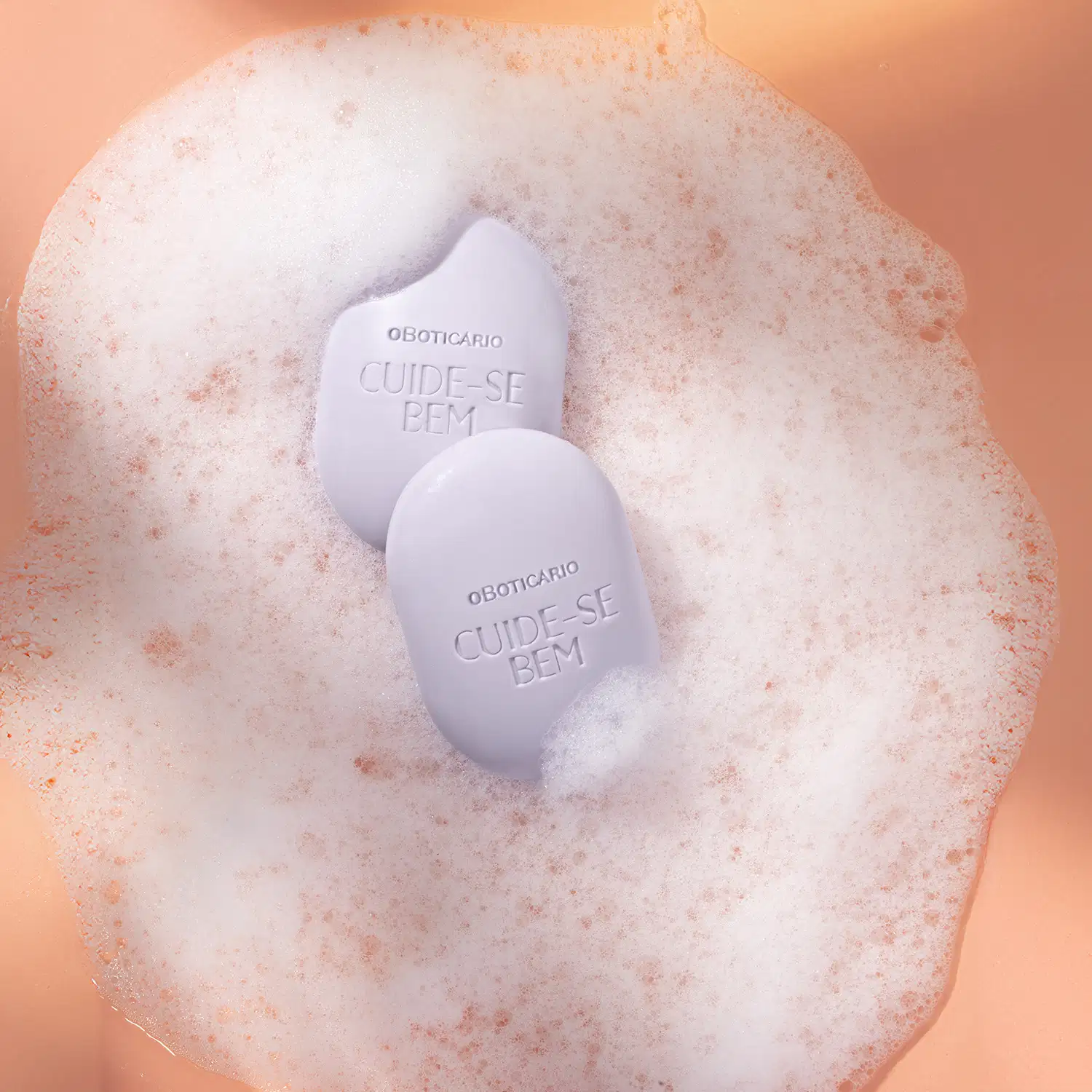 Dois sabonetes em barra azuis da marca Cuide-se Bem Boa Noite com muita espuma branca ao redor em fundo laranja.