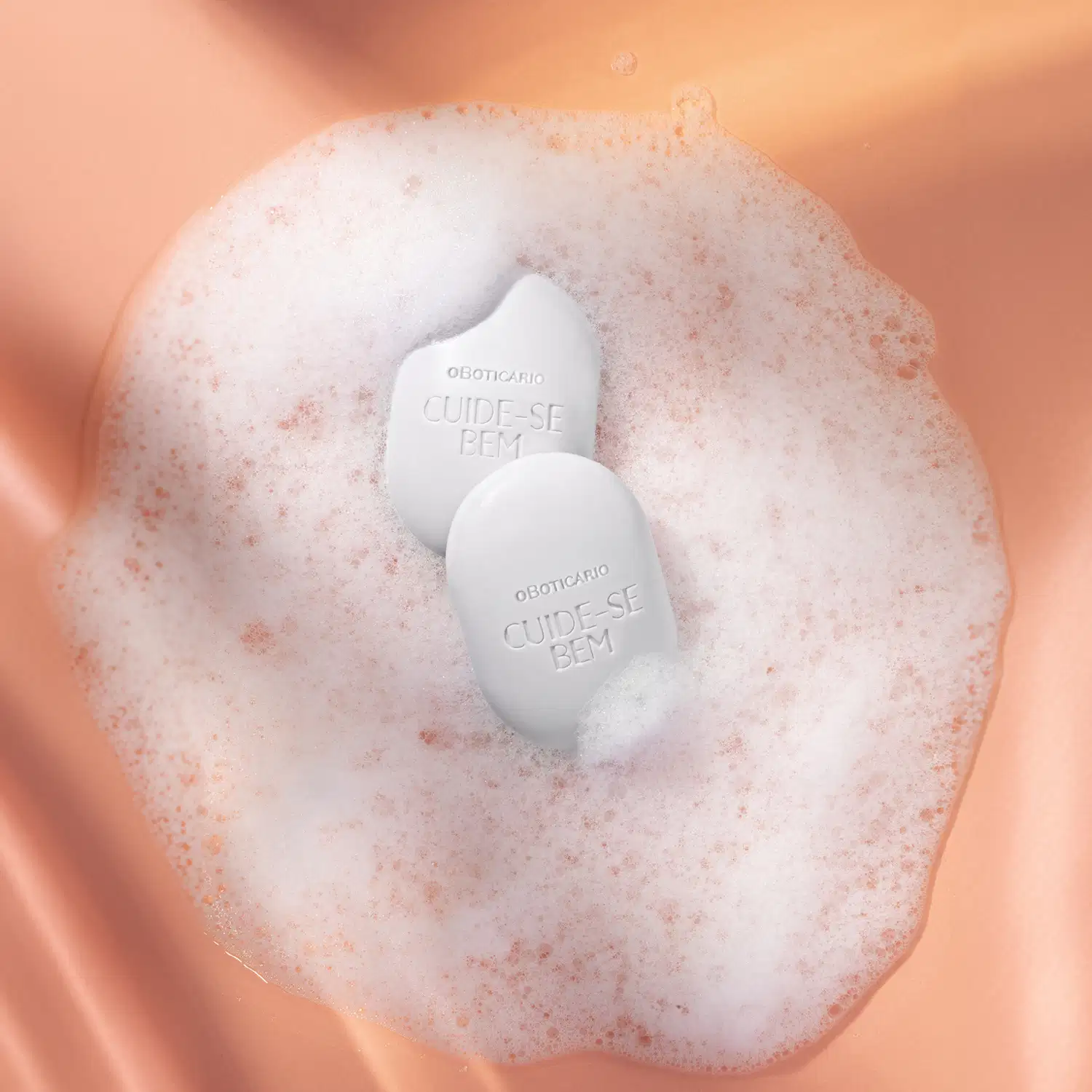 Dois sabonetes em barra azuis com muita espuma branca em volta em um fundo laranja ondulado.