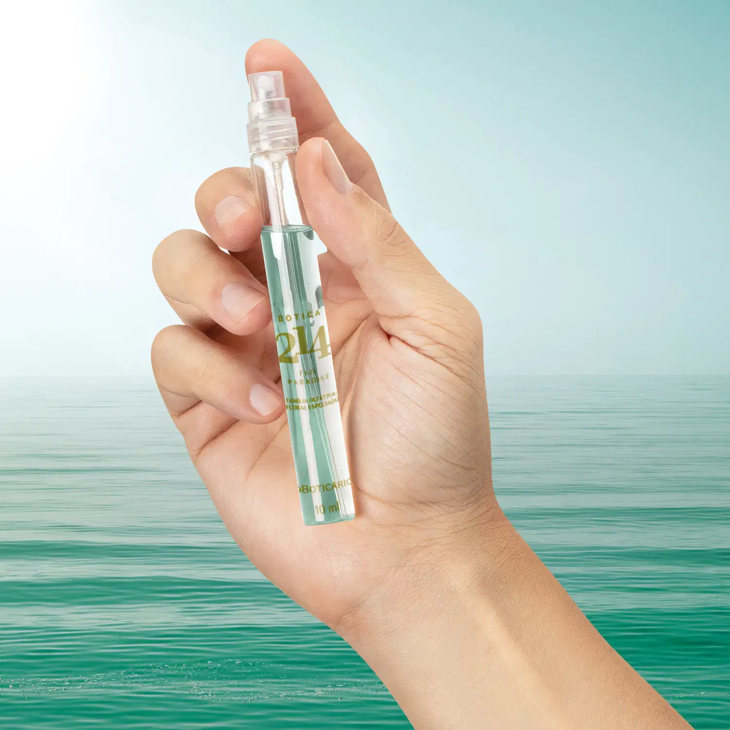 Vidro cilíndrico transparente com líquido azul claro, tampa preta e letras douradas contendo 10ml de Eau de Parfum feminino da marca Botica 214 Fiji Paradise. O fundo da imagem simula água e céu azul.