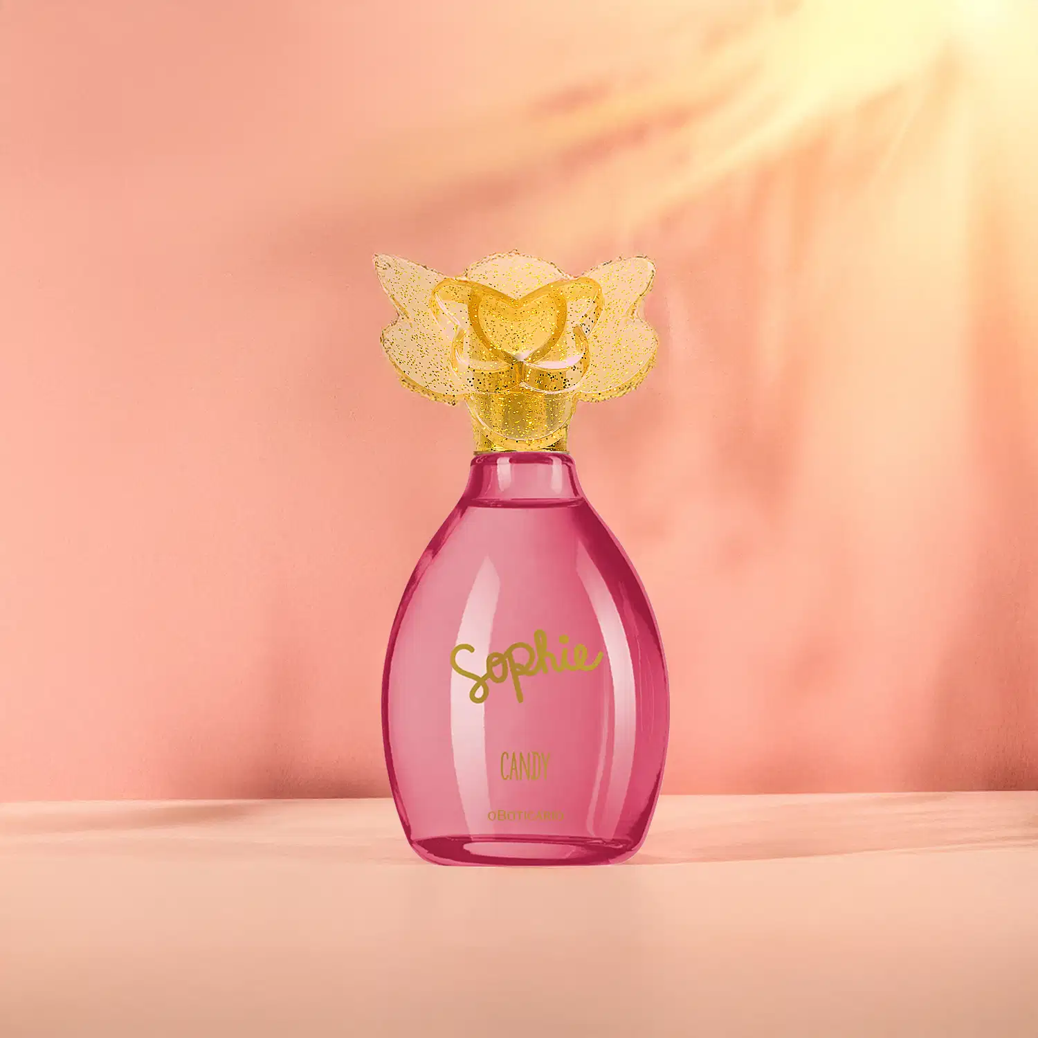 Frasco de colônia infantil Sophie Candy rosa com tampa dourada em formato de borboleta, sobre superfície clara em ambiente com iluminação suave e tons de laranja.s