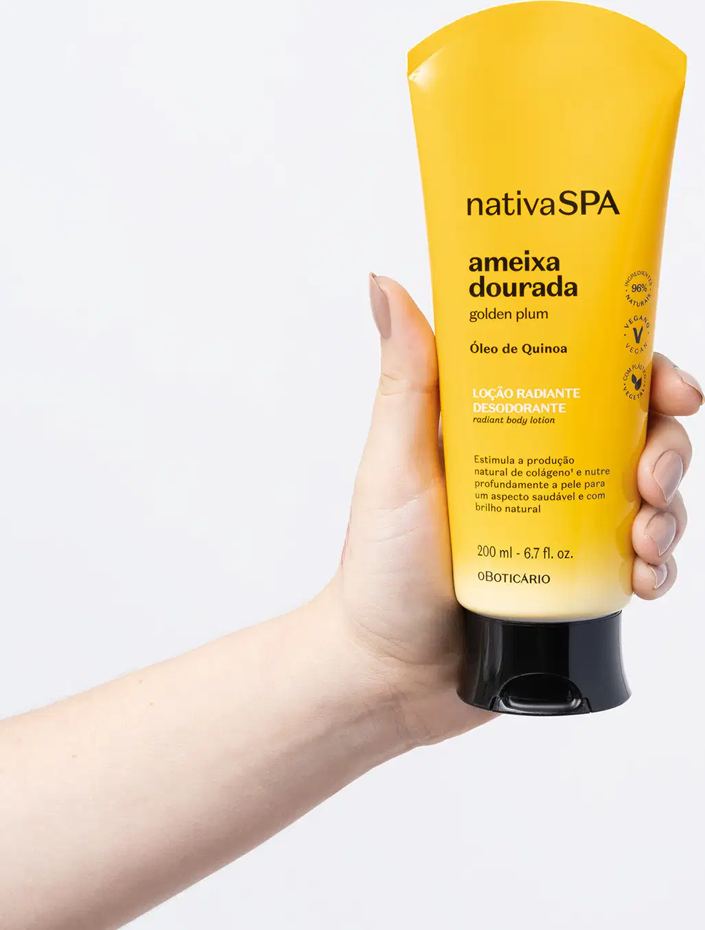 Mão segurando um frasco com degradê de amarelo e branco, tampa e letras pretas contendo loção radiante corporal Nativa SPA Ameixa Dourada em fundo azul claro.