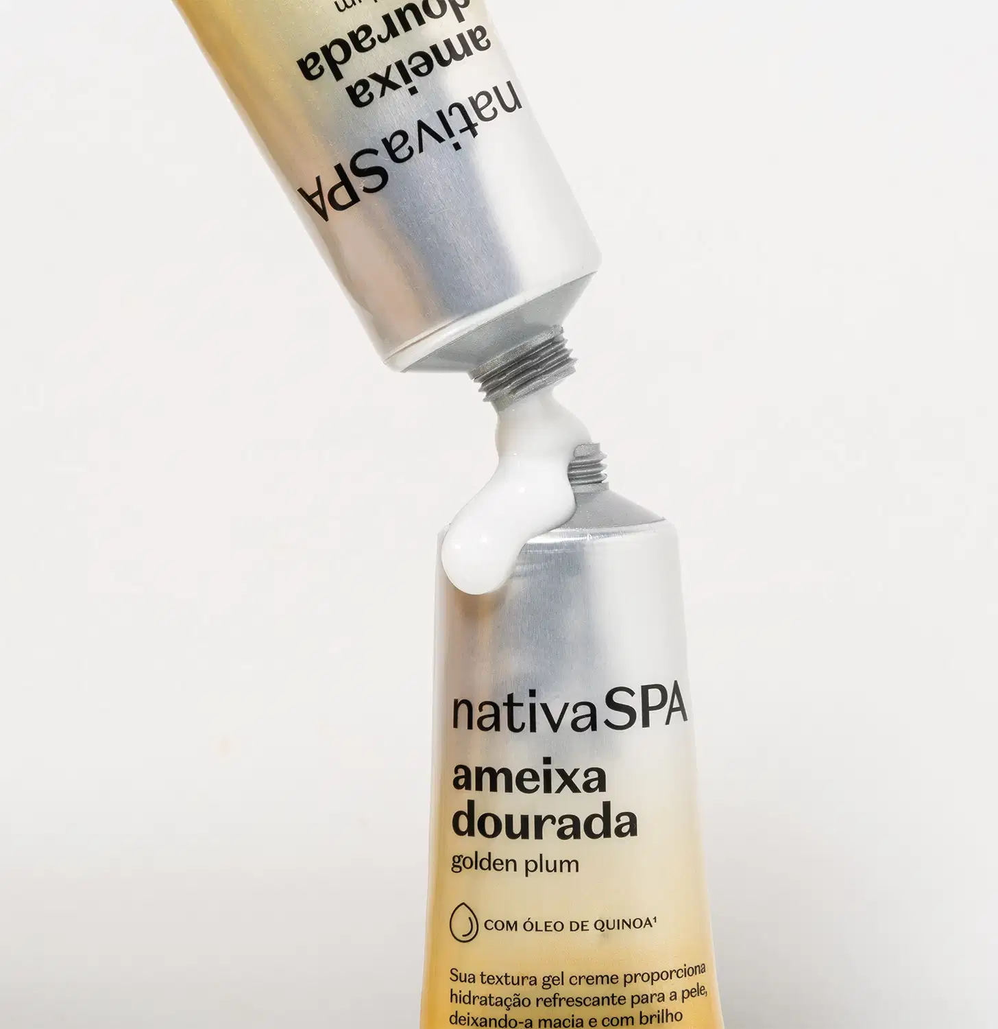 Duas bisnagas com degradê de prata e amarelo com letras pretas jogando gel creme para as mãos da marca Nativa SPA Ameixa Dourada uma sobre a outra em fundo cinza.