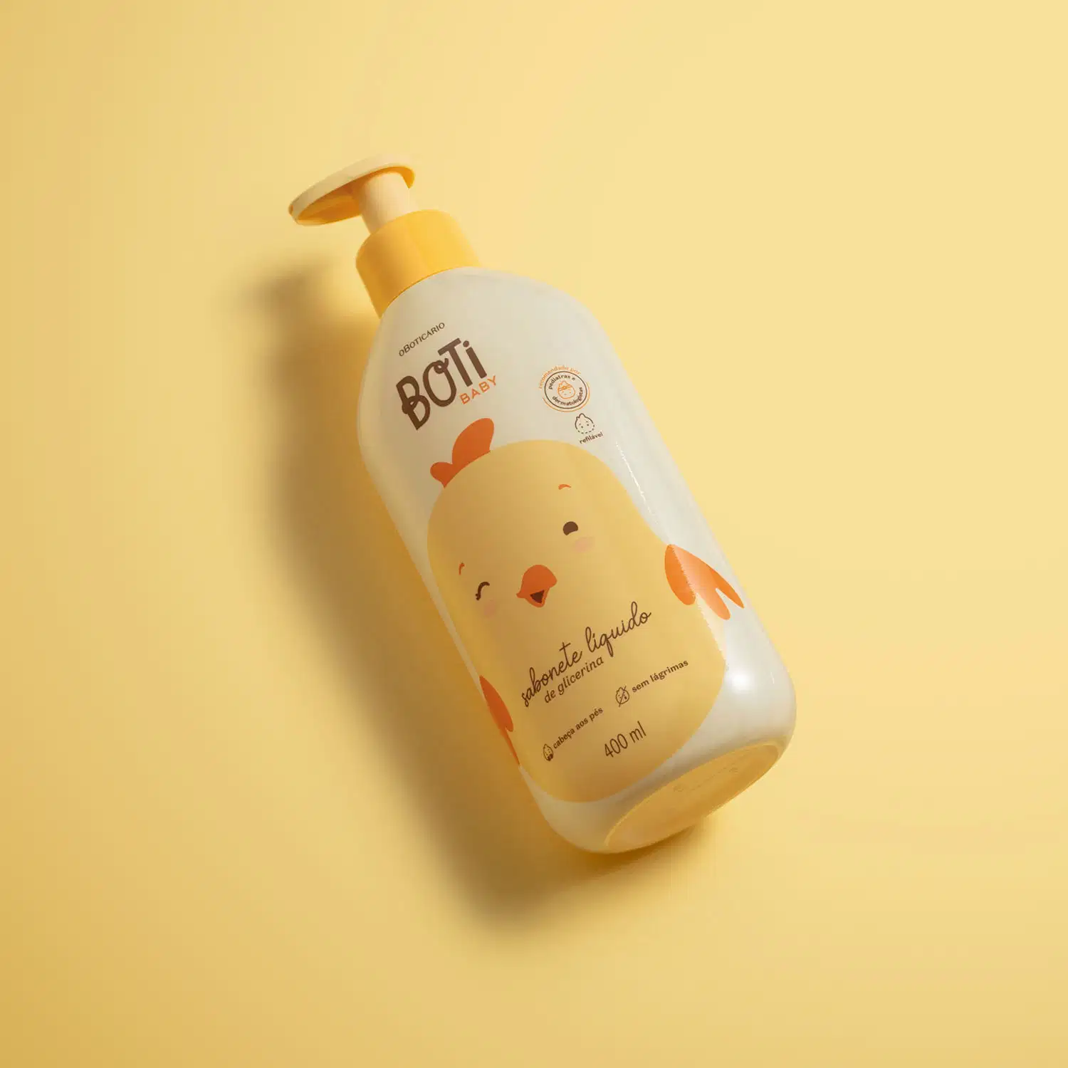 Frasco amarelo claro com ilustração de um passarinho amarelo com detalhes, tampa e bomba dosadora laranjas contendo sabonete líquido de glicerina da marca Boti Baby em fundo alaranjado.