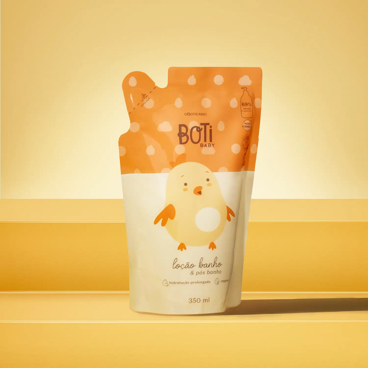 Refil de loção hidratante corporal da marca Boti Baby em forma de sachê nas cores laranja e amarelo claro com ilustração de passarinho amarelo. A imagem está em cima de uma plataforma laranja com fundo e superfície em tons alaranjados.
