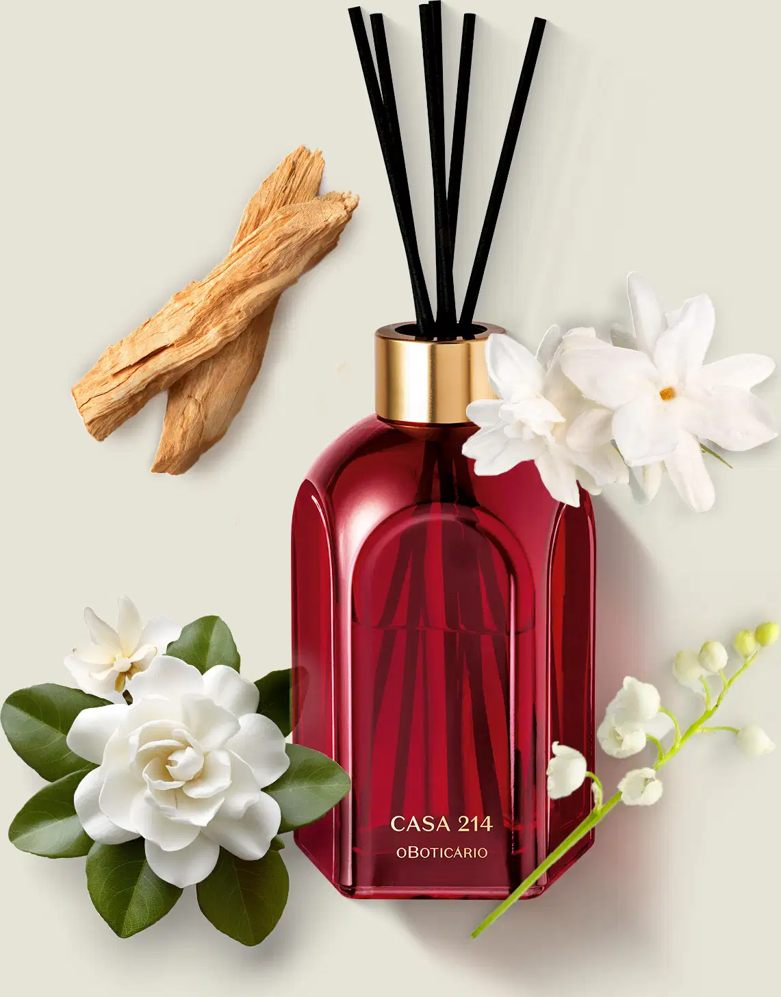 Difusor de ambientes em vidro vermelho com varetas e letras douradas da marca Casa 214 Gardênia Imperial sobre superfície clara com flores brancas e galhos de madeira.