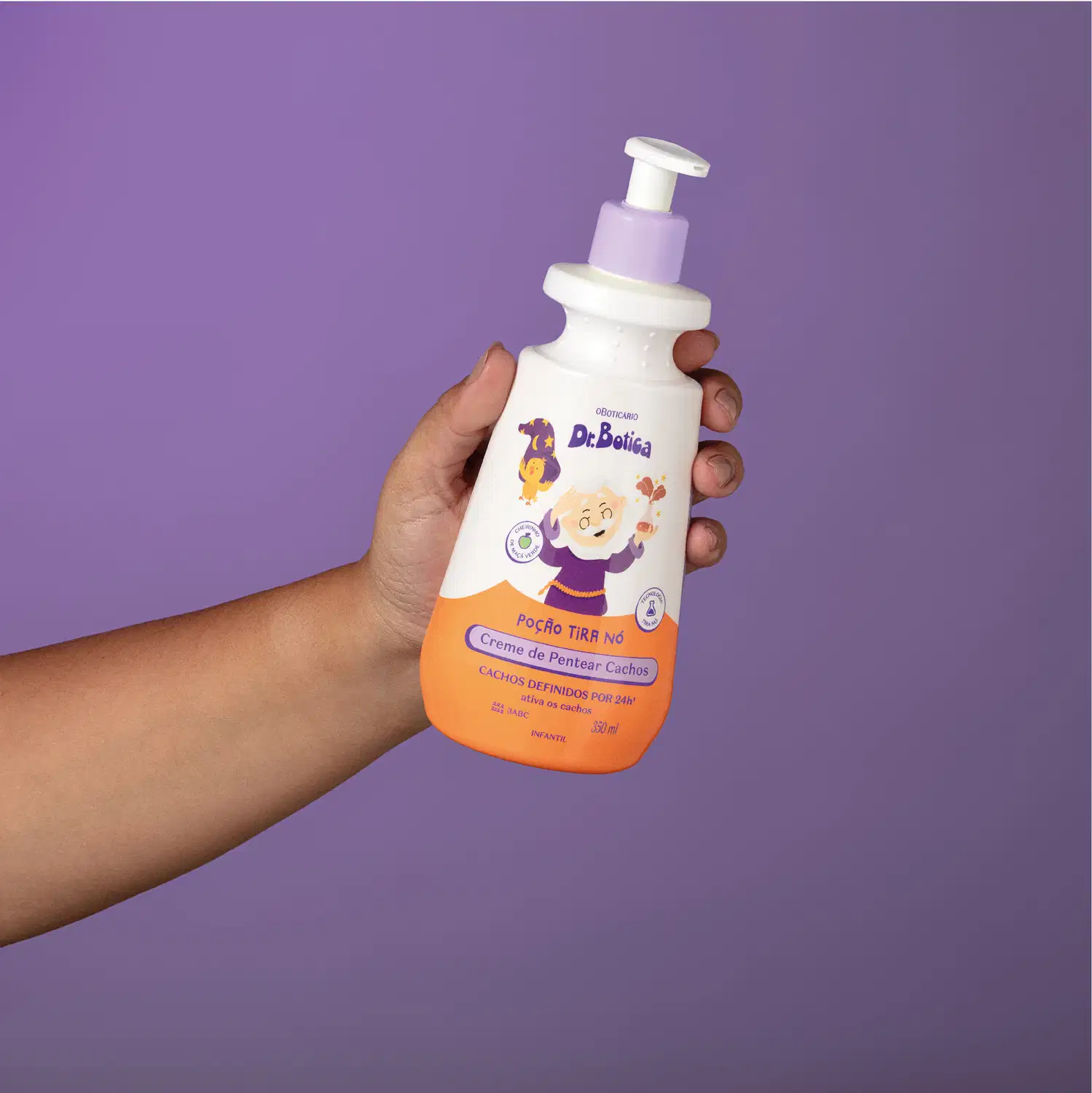 Imagem de uma mão segurando uma embalagem branca e laranja com válvula dosadora roxa de creme de pentear infantil para cabelos cacheados da marca Dr. Botica em fundo azul escuro.