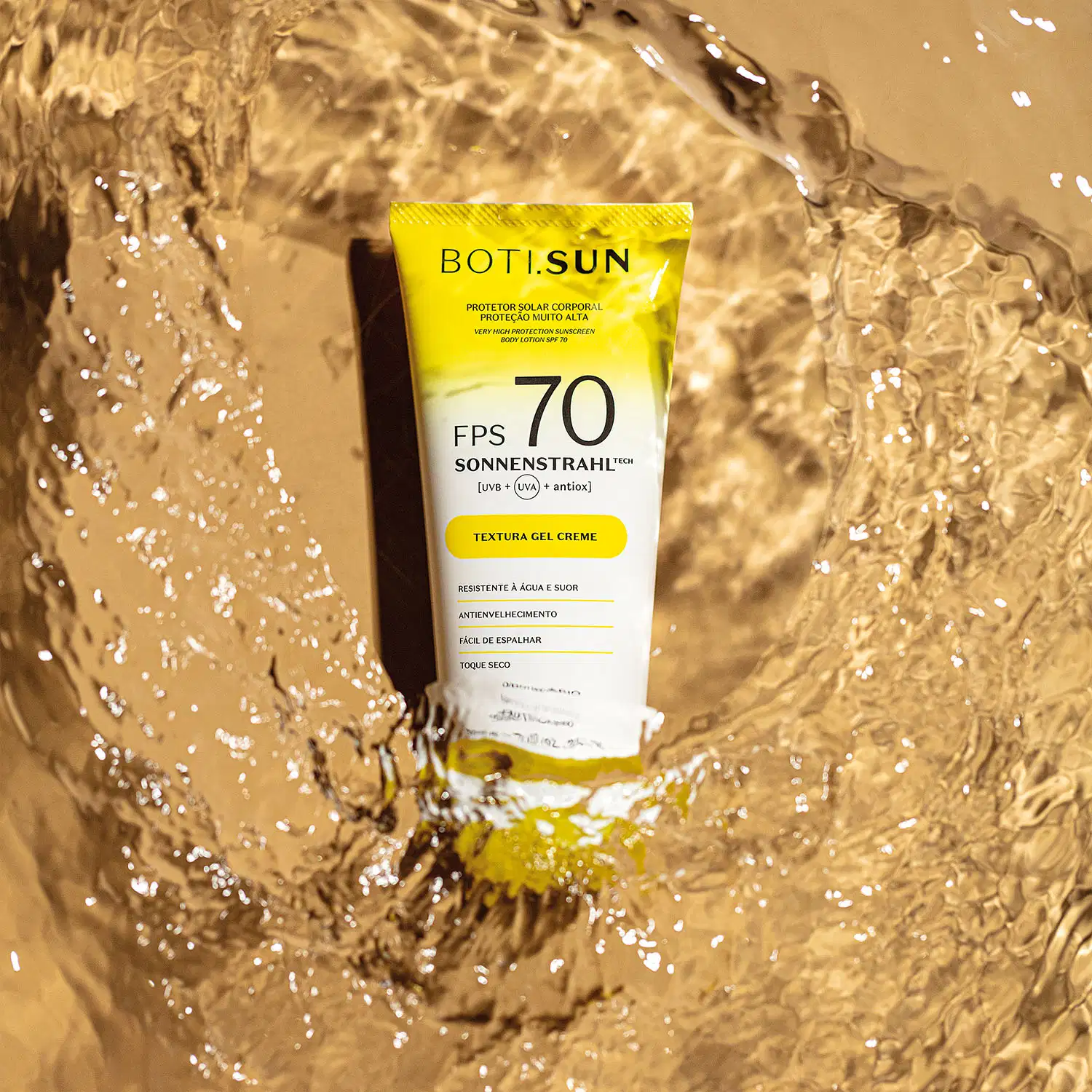Bisnaga amarela e branca com tampa amarela e letras pretas de protetor solar corporal FPS 70 da marca Boti.Sun em um cenário d areia de praia molhada.